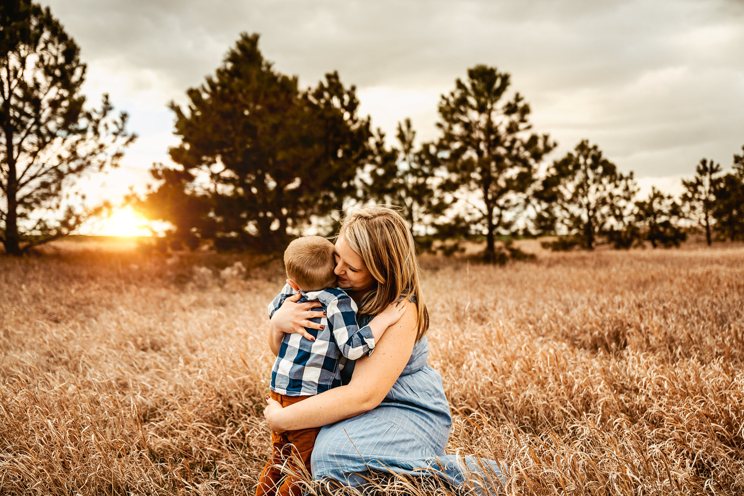 Mom and son hug each other while sitting on the ground with open field and trees