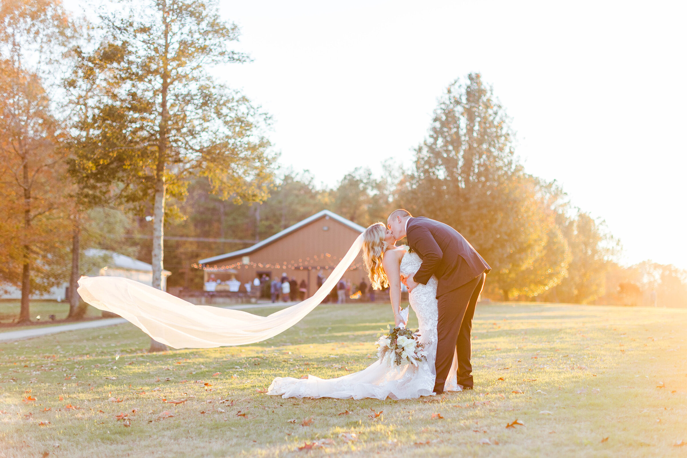 A groom wearing a blue suit dipping and kissing his fiance wearing a white satin dress with a slit and bow kissing her neck while she giggles in front of the Nashville War Memorial by nashville wedding photographer, Brooke Elliott