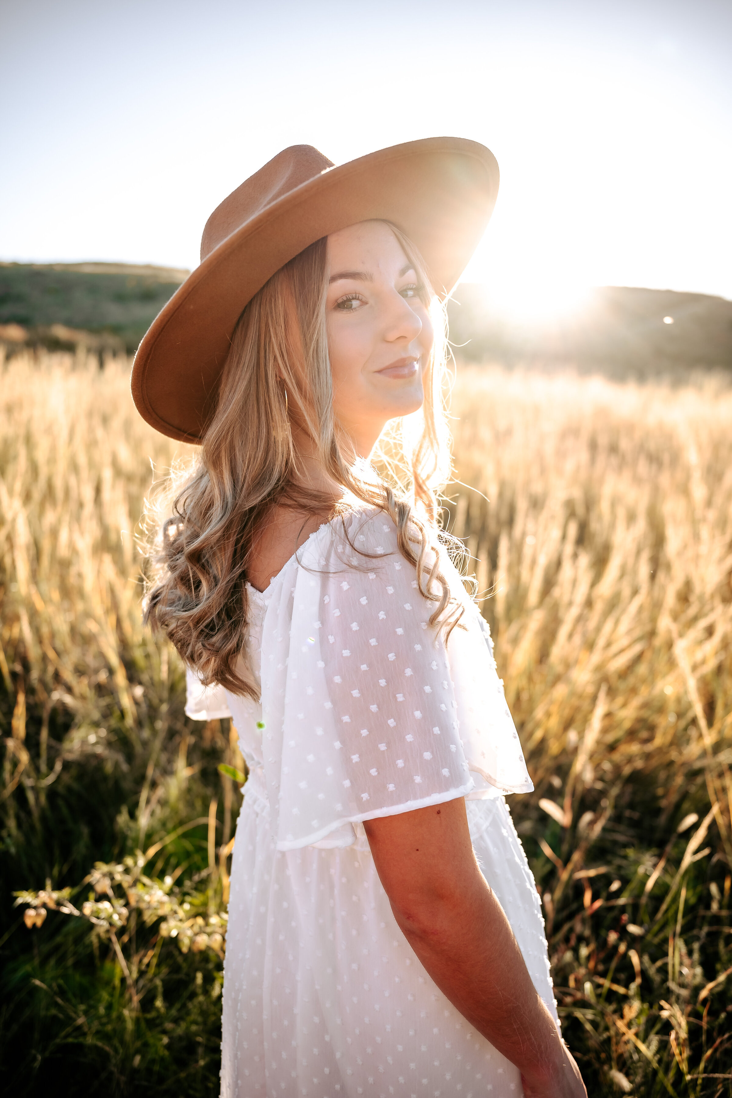 girl smiles over her shoulder in white dotted dress and wide brim felt hat in Nebraska