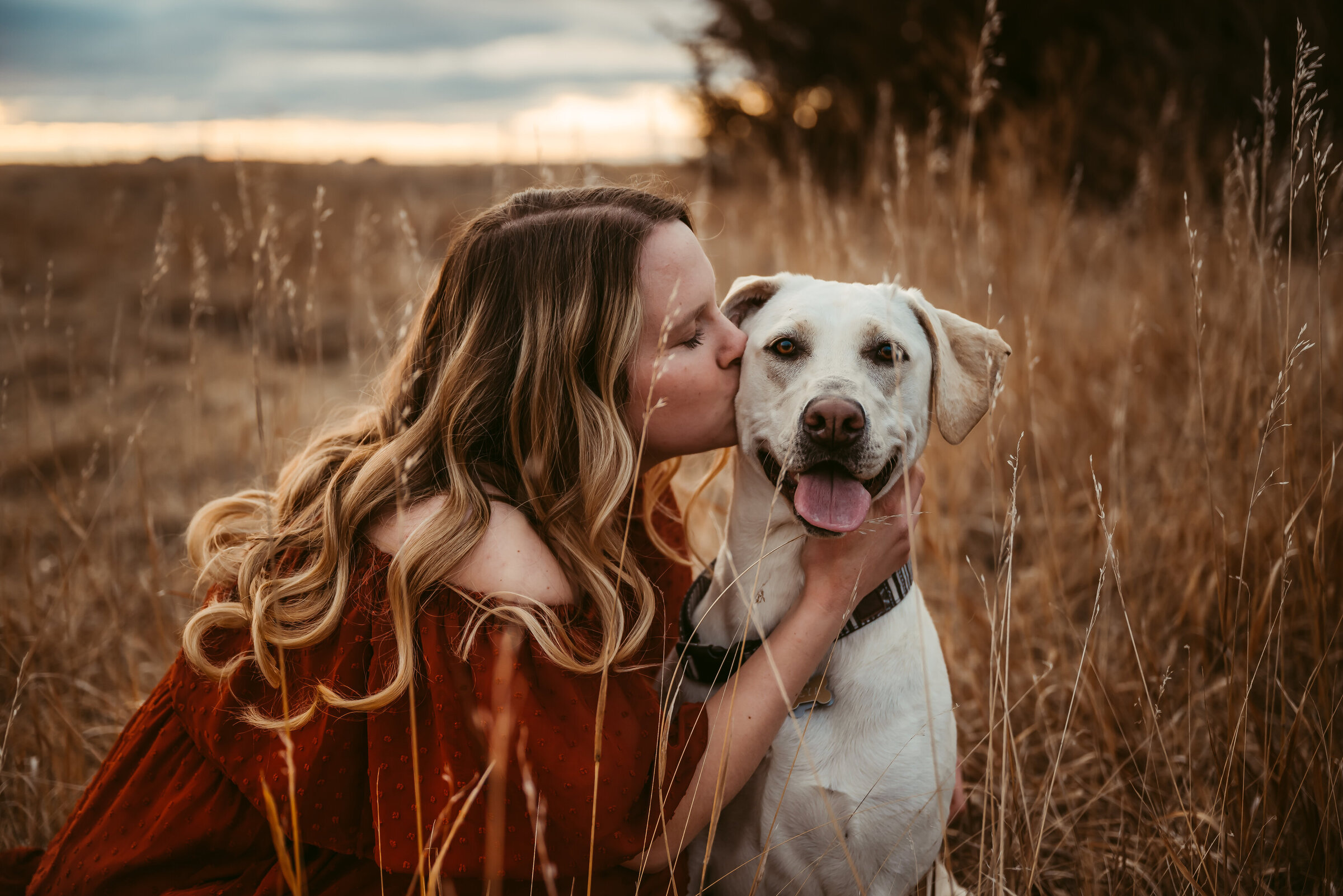 Woman kisses smiling dog on the cheek while dog pants and smiles at the camera