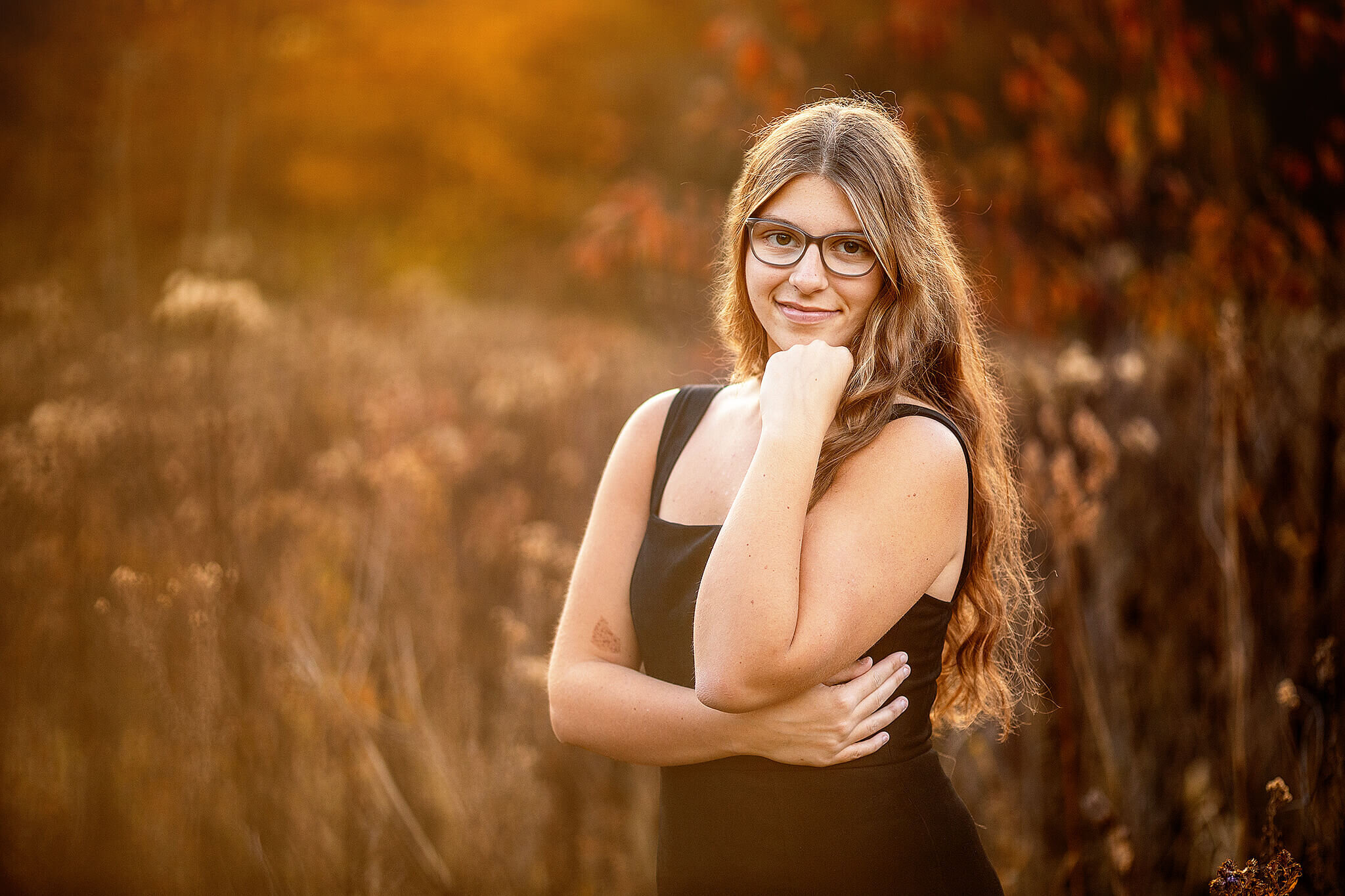 marion Ohio high school senior standing in front of field in the fall wearing a black dress at gorman nature center in lexington ohio