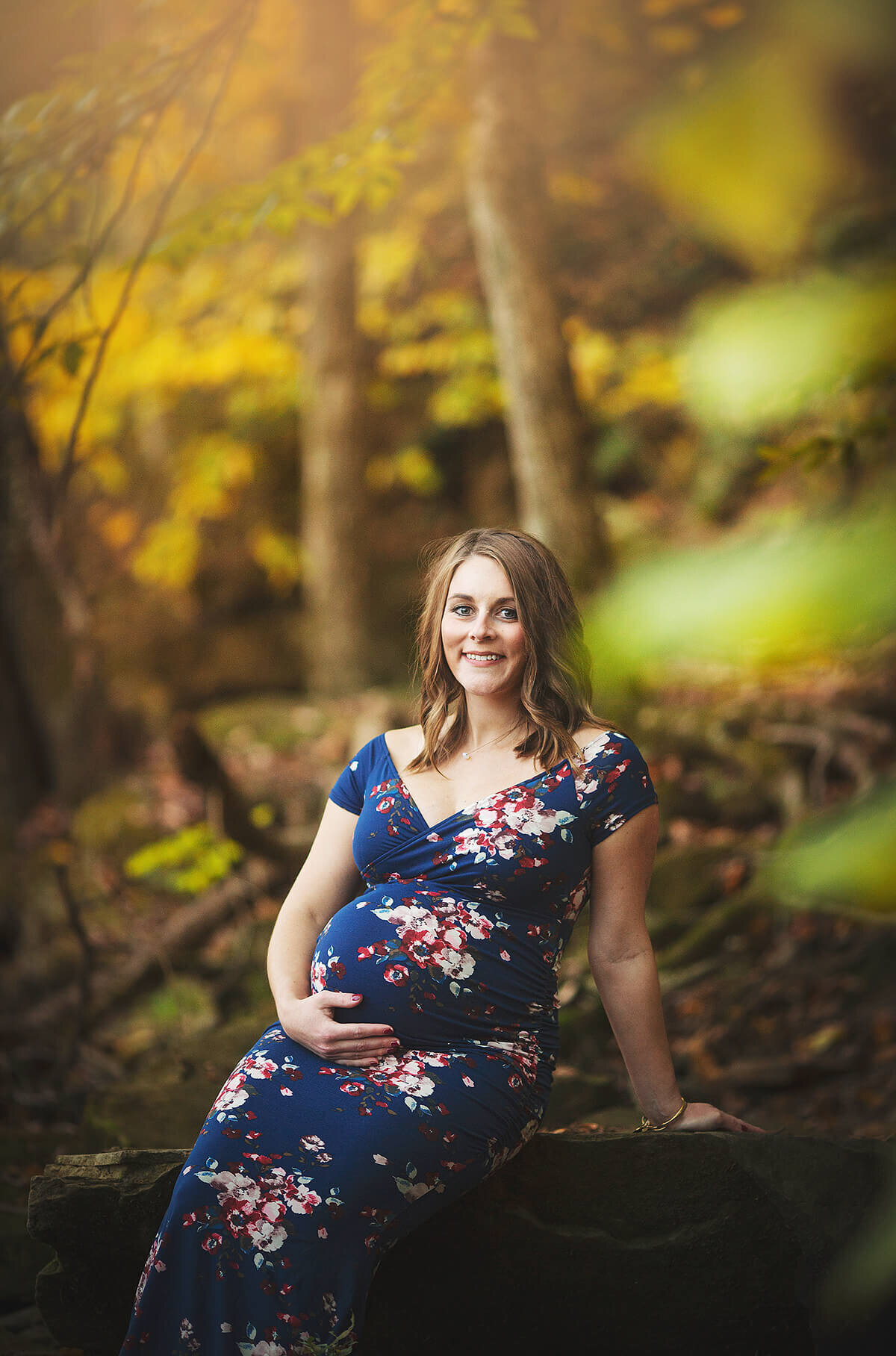 Pregnant women in blue dress with flowers on it, sitting on rock at Lowe Volk Park