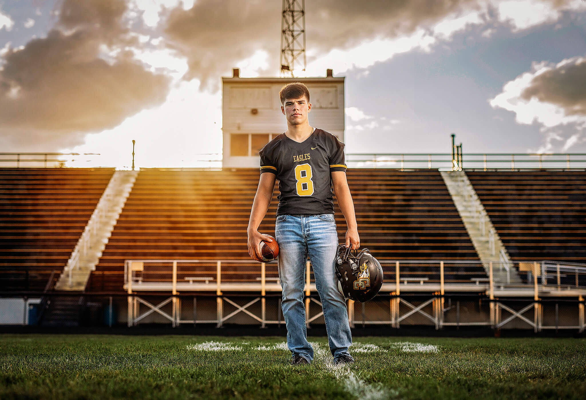 high school senior boy standing in front of football stands with helmet and football in hand at Colonel Crawford high school