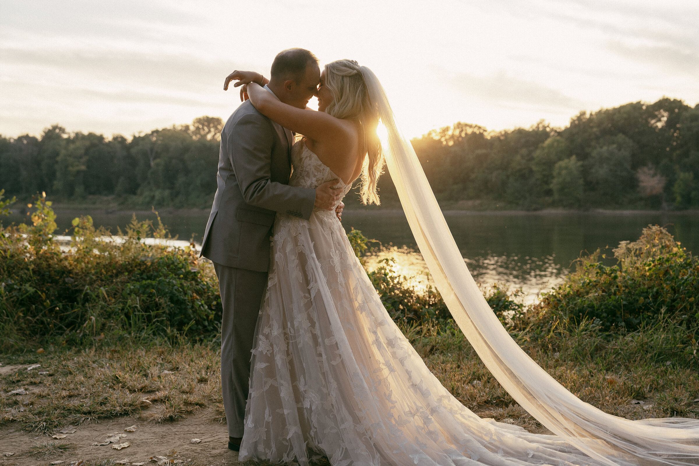 Wedding couple kissing with sunlight flare by the lake.