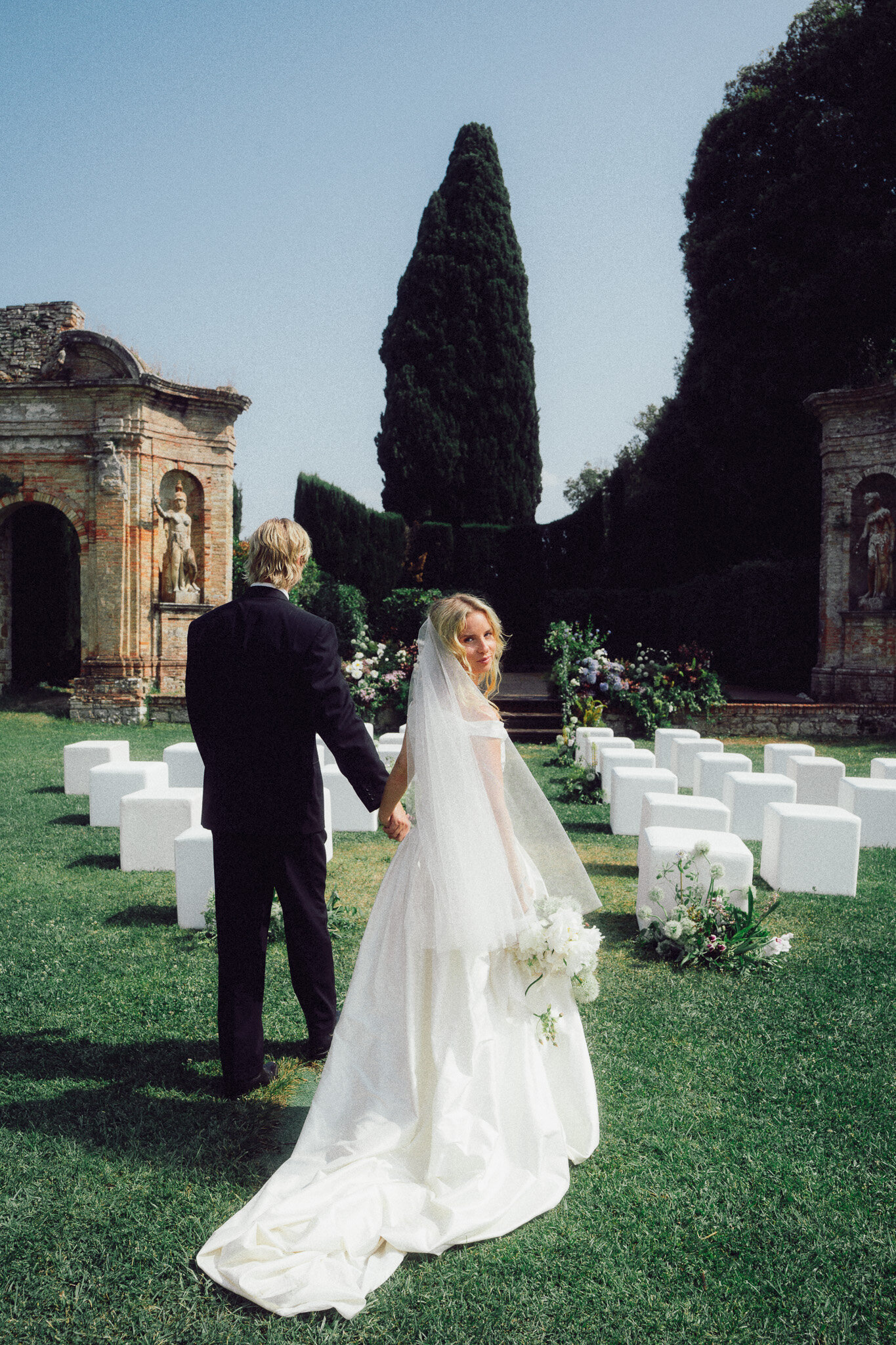 Bride and groom walking through an elegant outdoor ceremony space in Italy, captured in a romantic, cinematic style by a luxury destination wedding photographer UK.