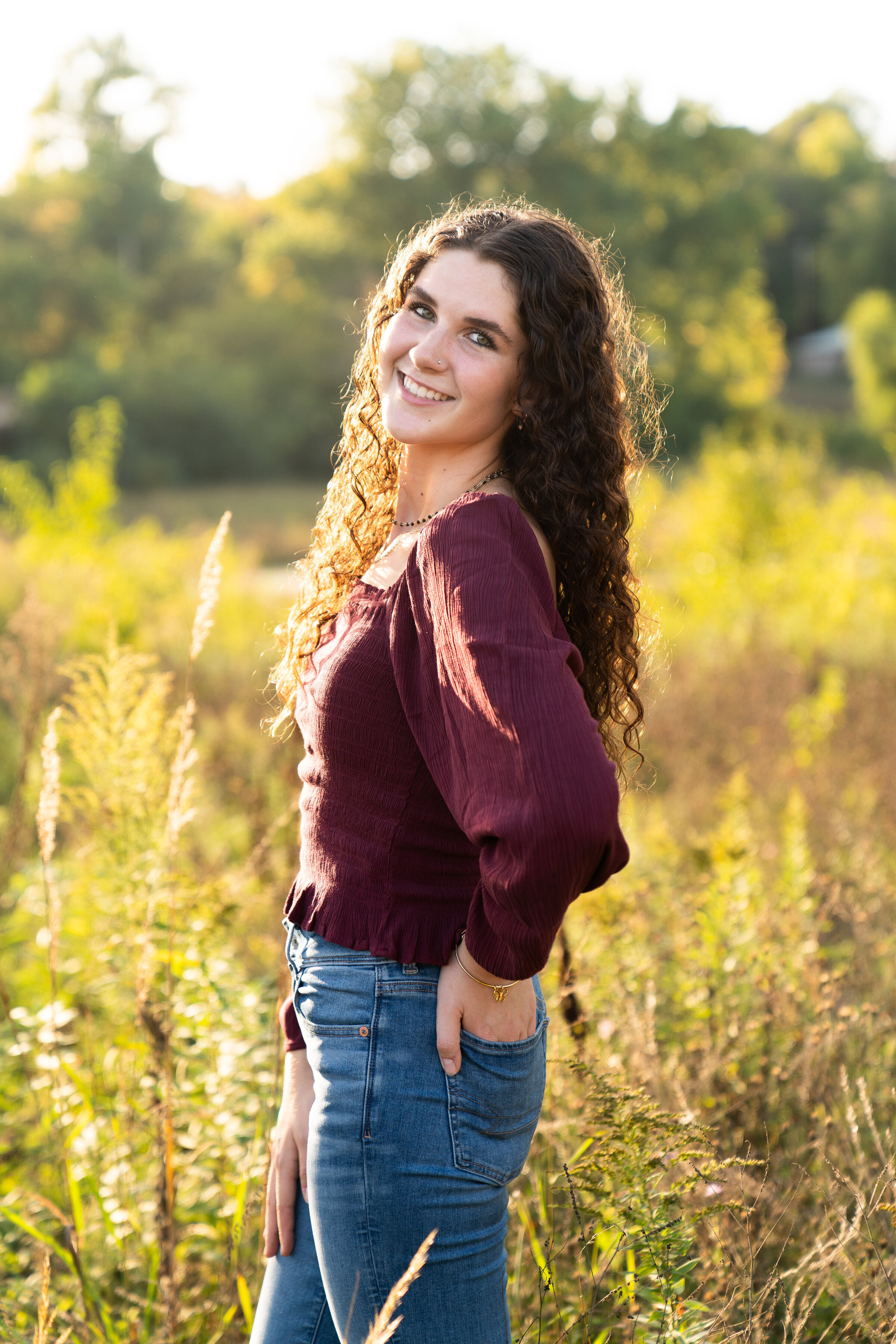 Girl poses in a field and smiles at the camera for her senior pictures.