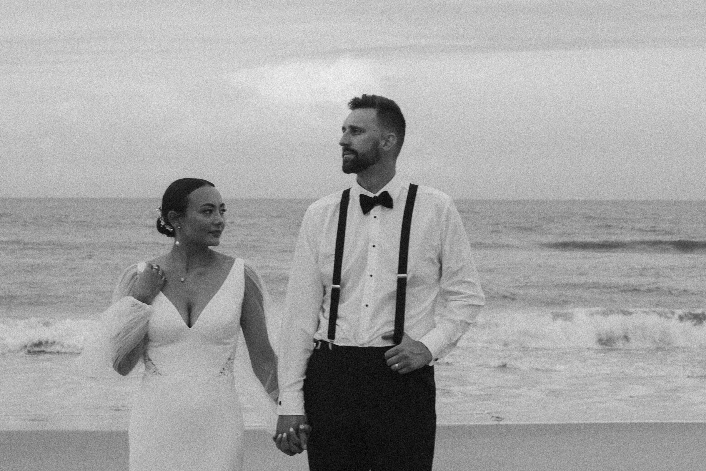 Bride and groom holding hands on the beach, black and white photo.