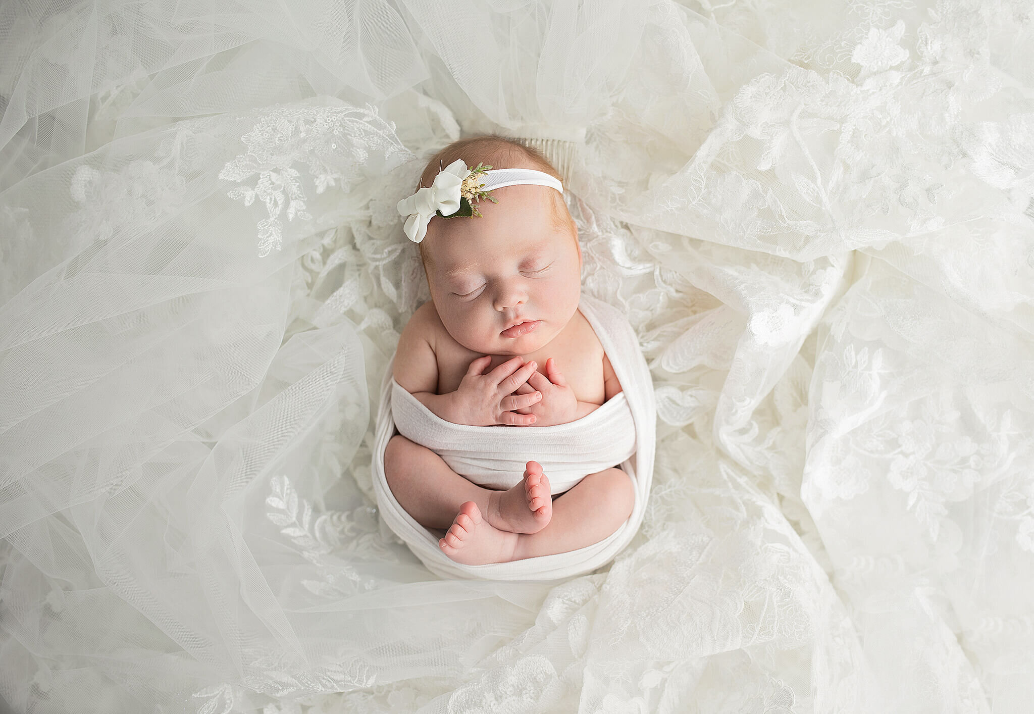 newborn baby girl wrapped in white and laying on moms wedding dress