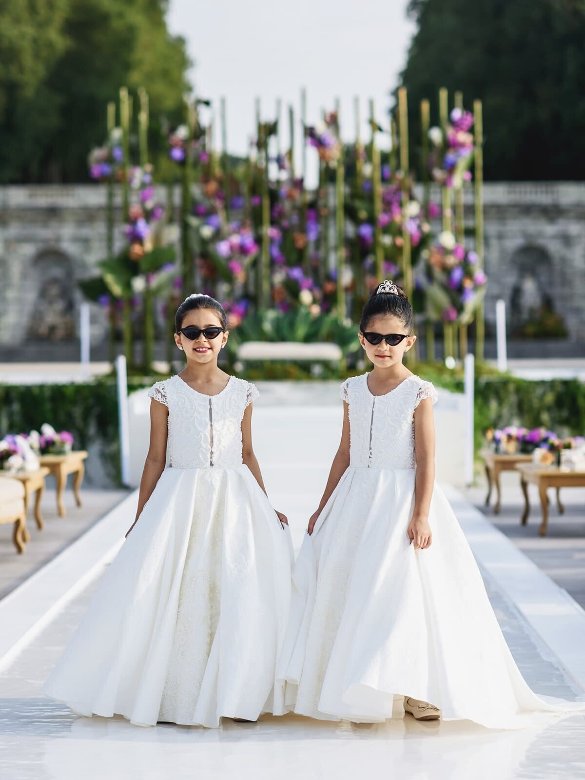 Two young girls in white dresses walking down wedding aisle
