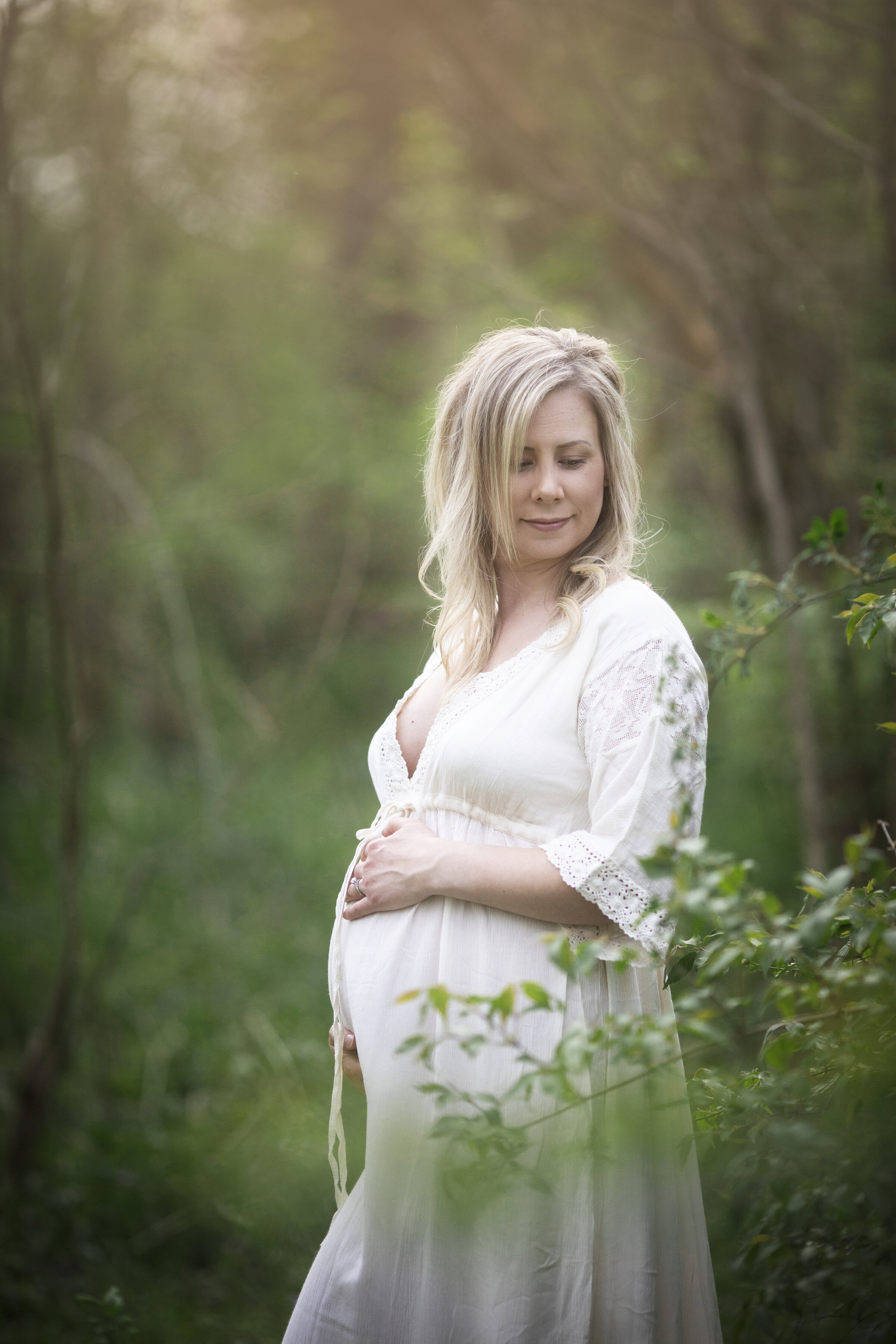 Pregnant women in white dress posed in front of a  spring woodsy area in bucyrus ohio , photo done by Erica Finnan Photography