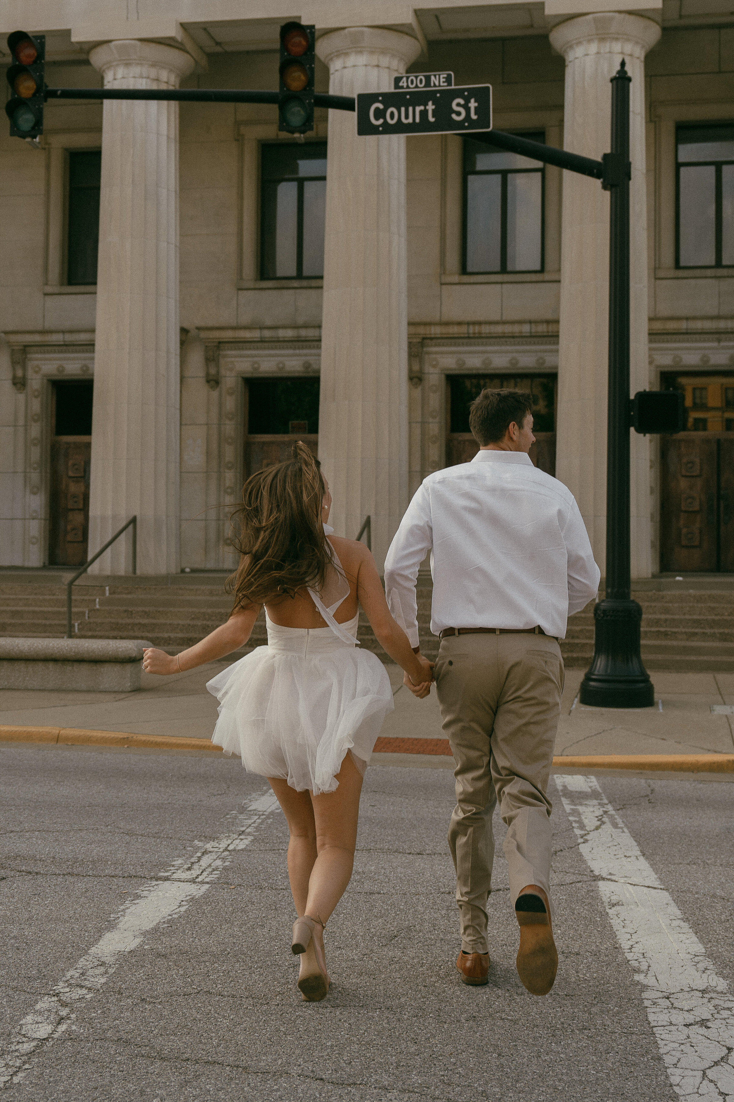 Joyful couple running across the street in casual wedding attire.