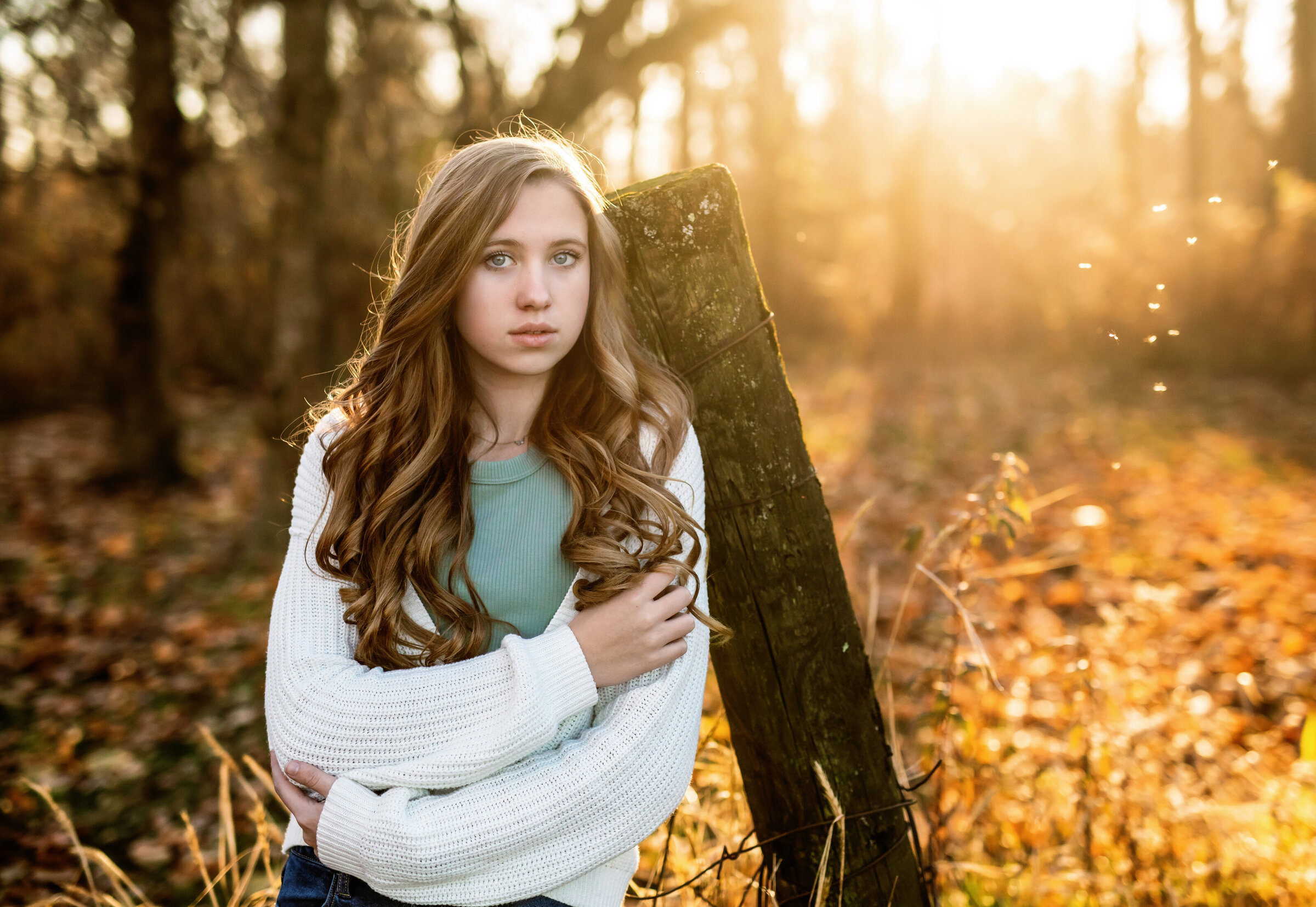 Teen girl standing against old wood post in woods while crossing her arms