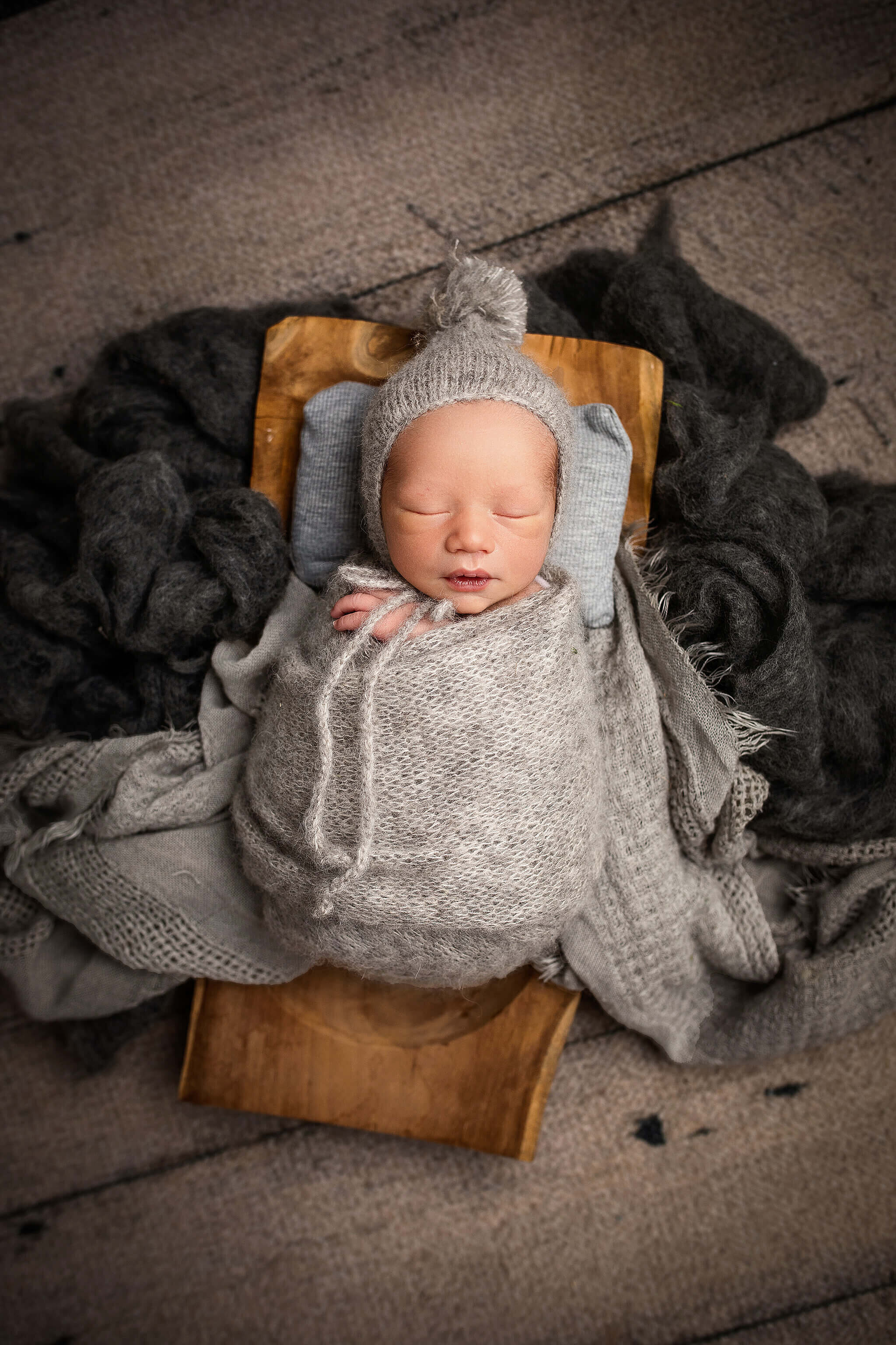 Newborn photo of baby boy wrapped in grey knit wrap with a cute grey hat with  poof on the top of the hat.