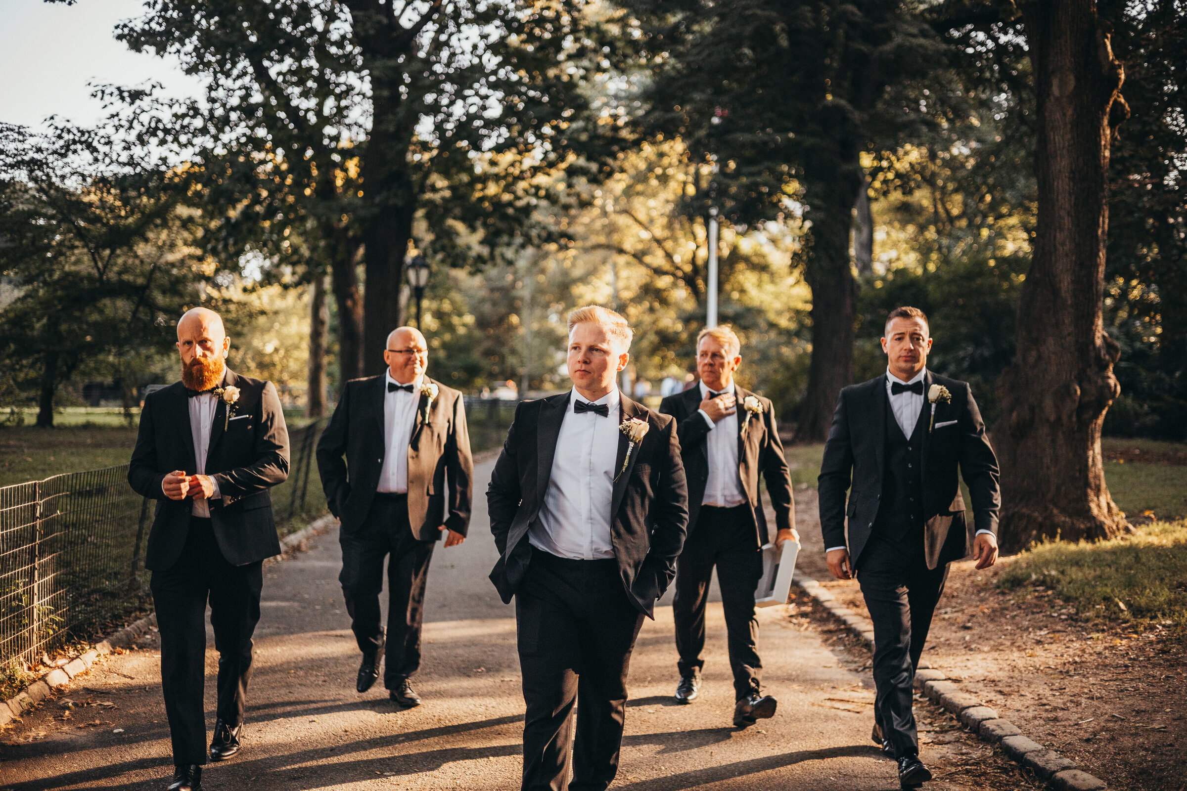 Groom and groomsmen in Tuxedos walking through central park