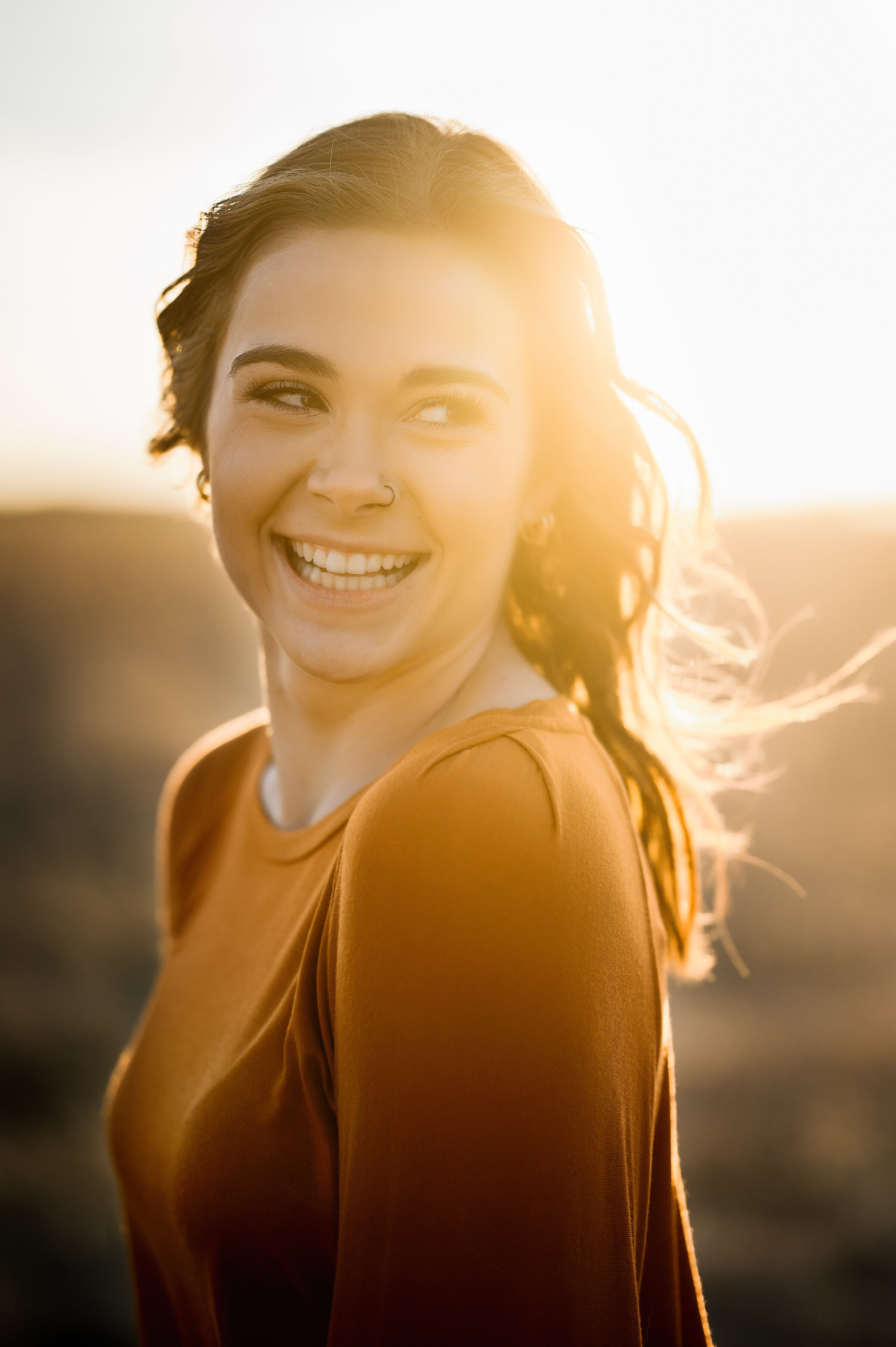 Senior laughs while looking over her shoulder at sunset