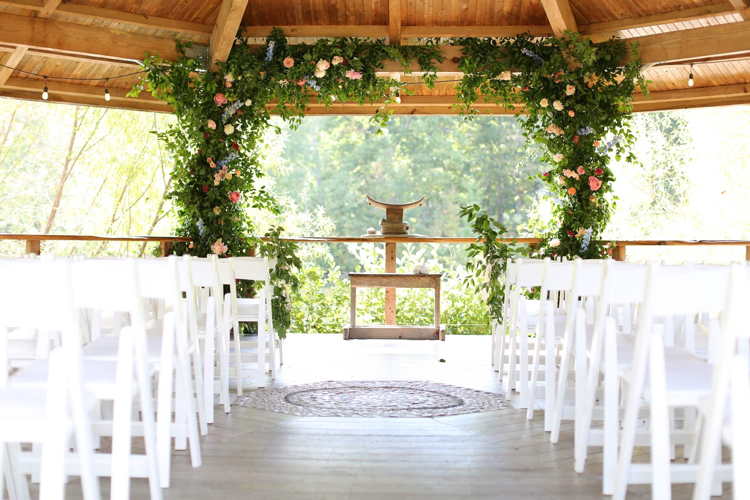 gazeebo wedding ceremony, white chairs, greenery and orange flowers rectangle arch.