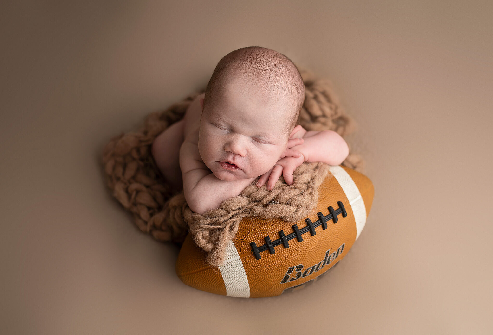newborn baby boy laying on football in bucyrus ohio photography studio