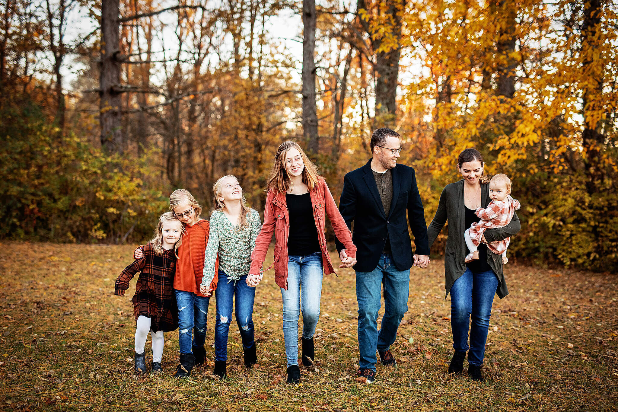 Family of seven holding hands and walking during fall photo session by Erica Finnan Photography