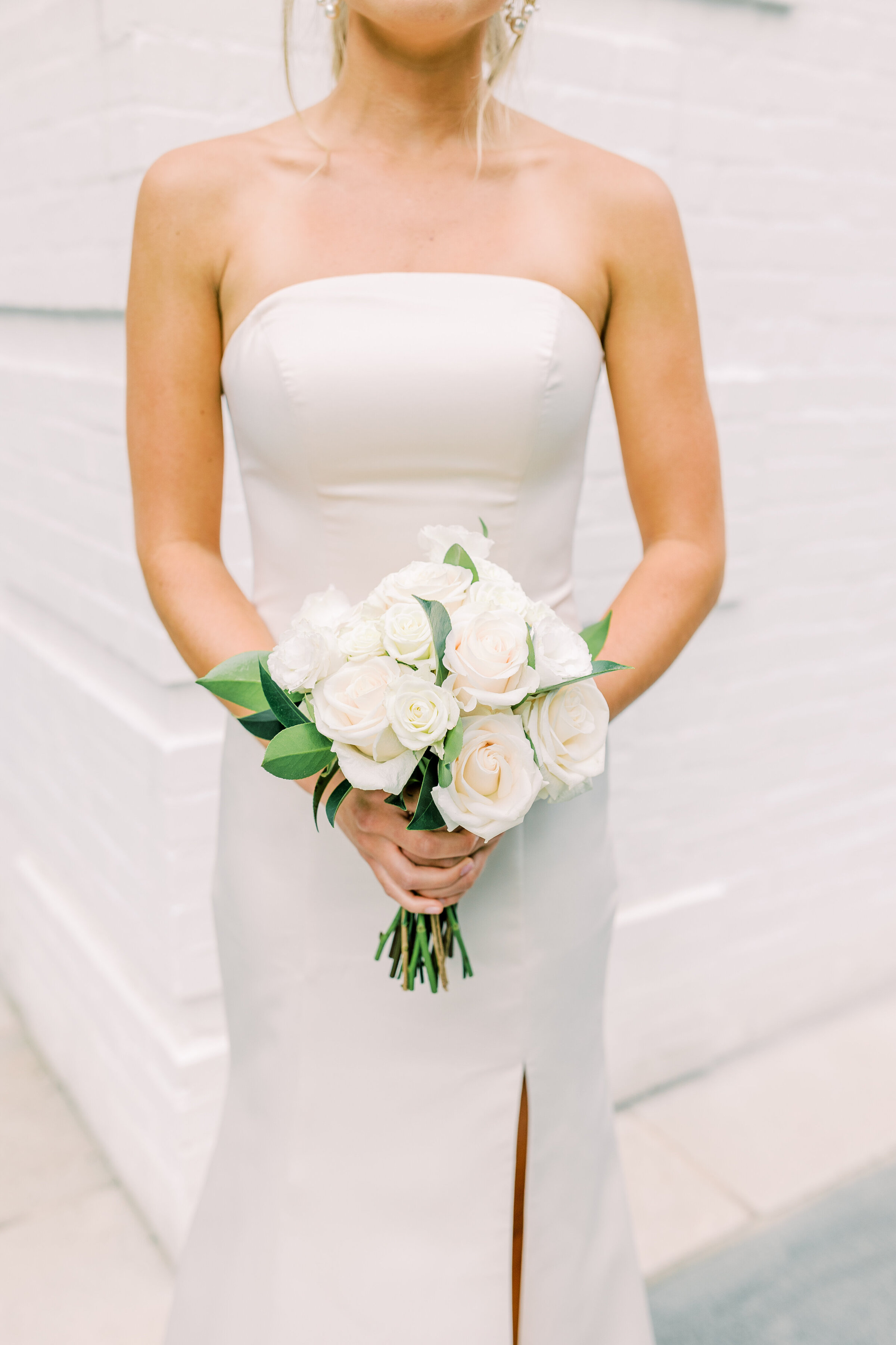 Bride in column style wedding dress holding white rose bouquet