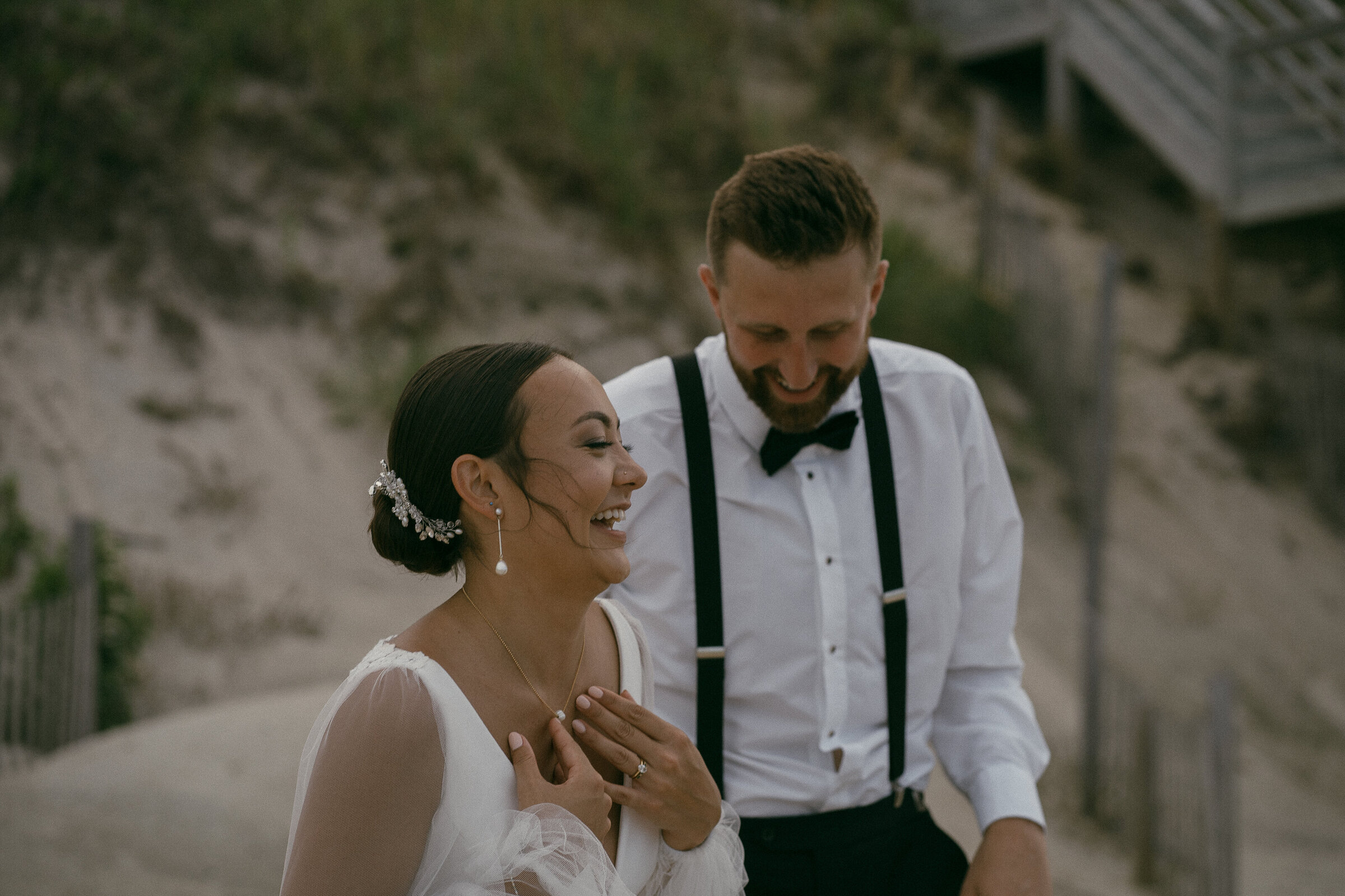 A laughing bride and groom walking on a sandy beach.