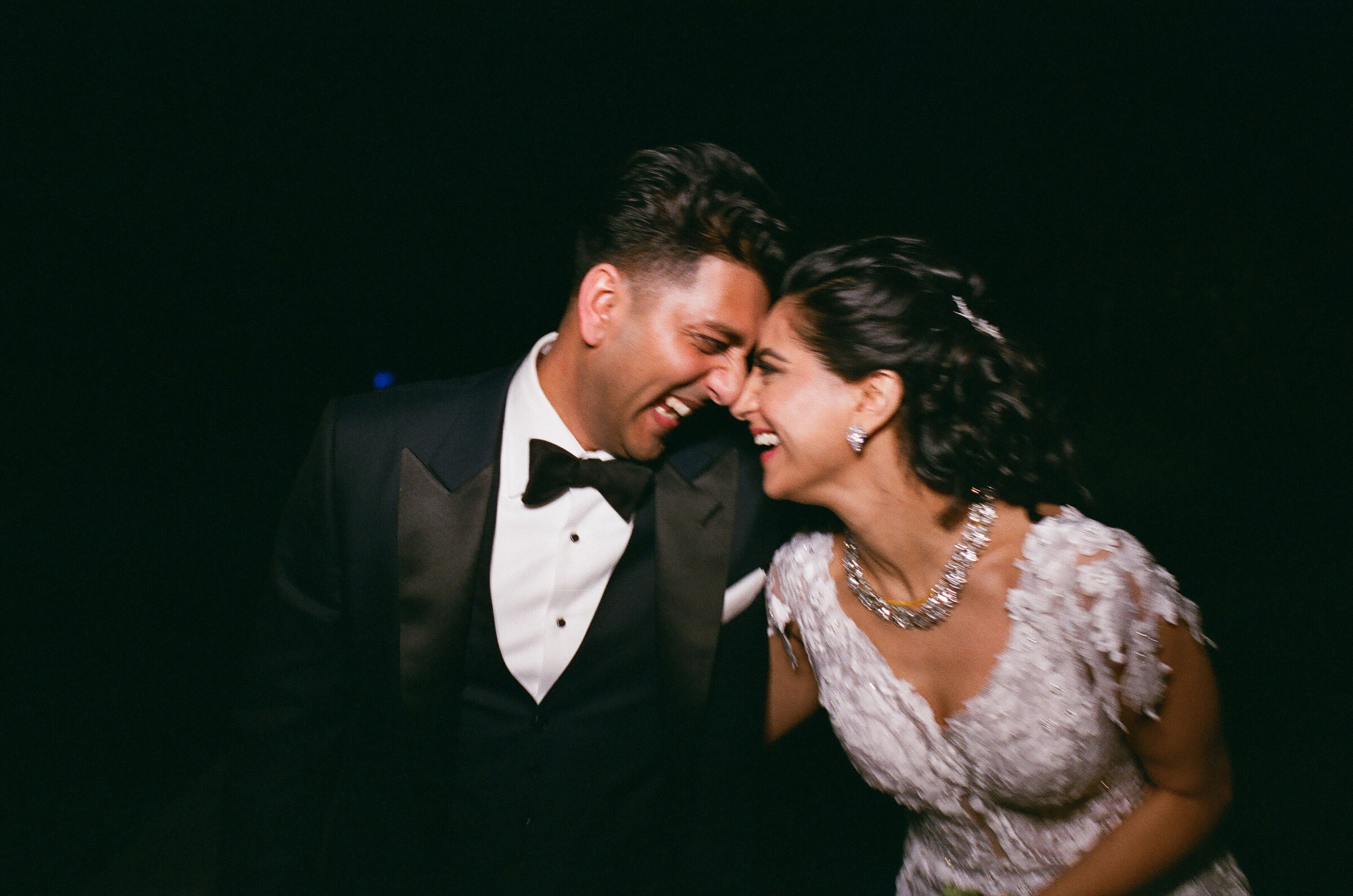 A wedding couple leaning in and touching foreheads as they laugh.