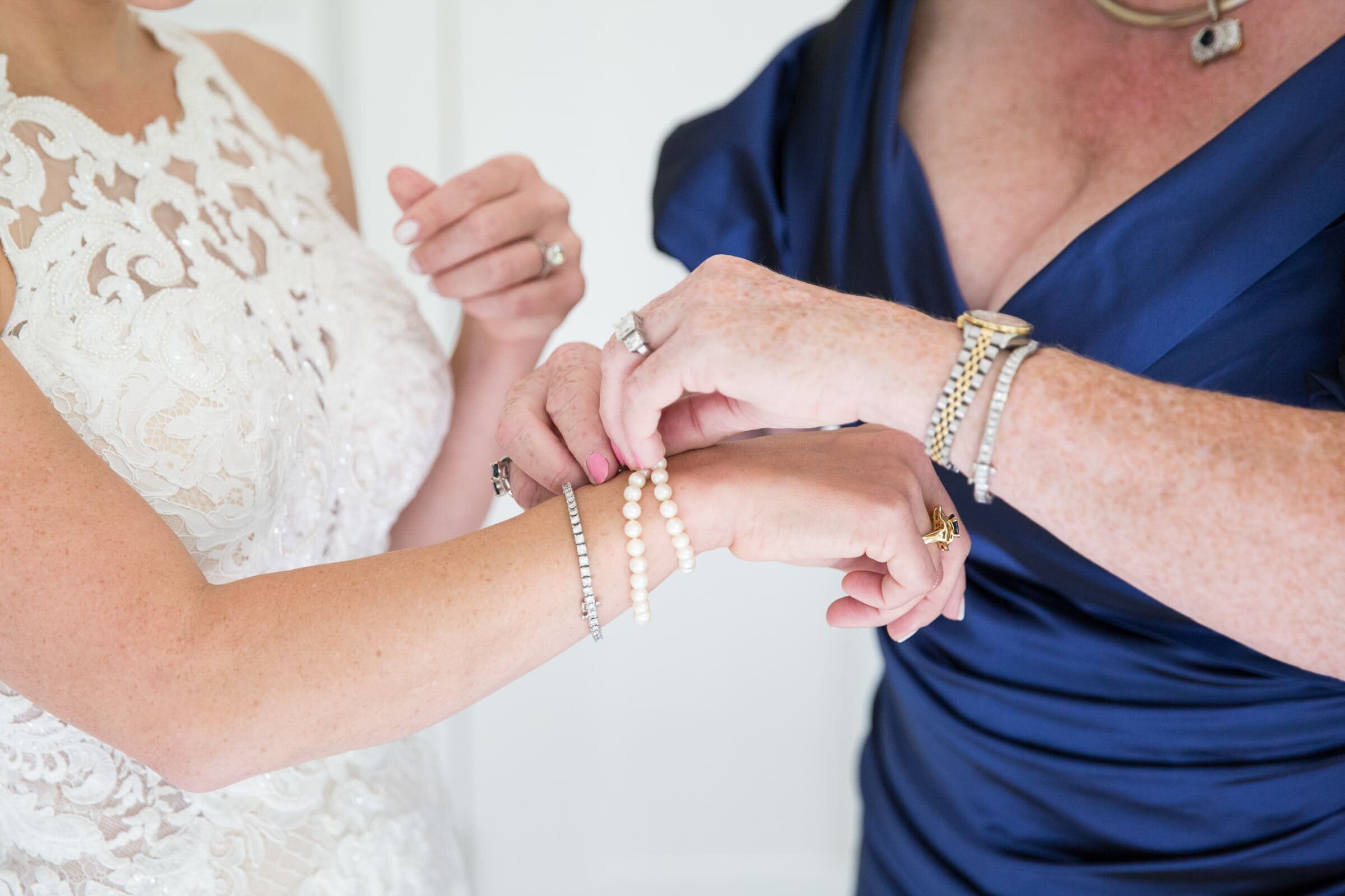 bright and airy wedding photography in Raleigh, NC. Mother of the bride putting on a pearl bracelet on her daughter wrist during bridal getting ready.