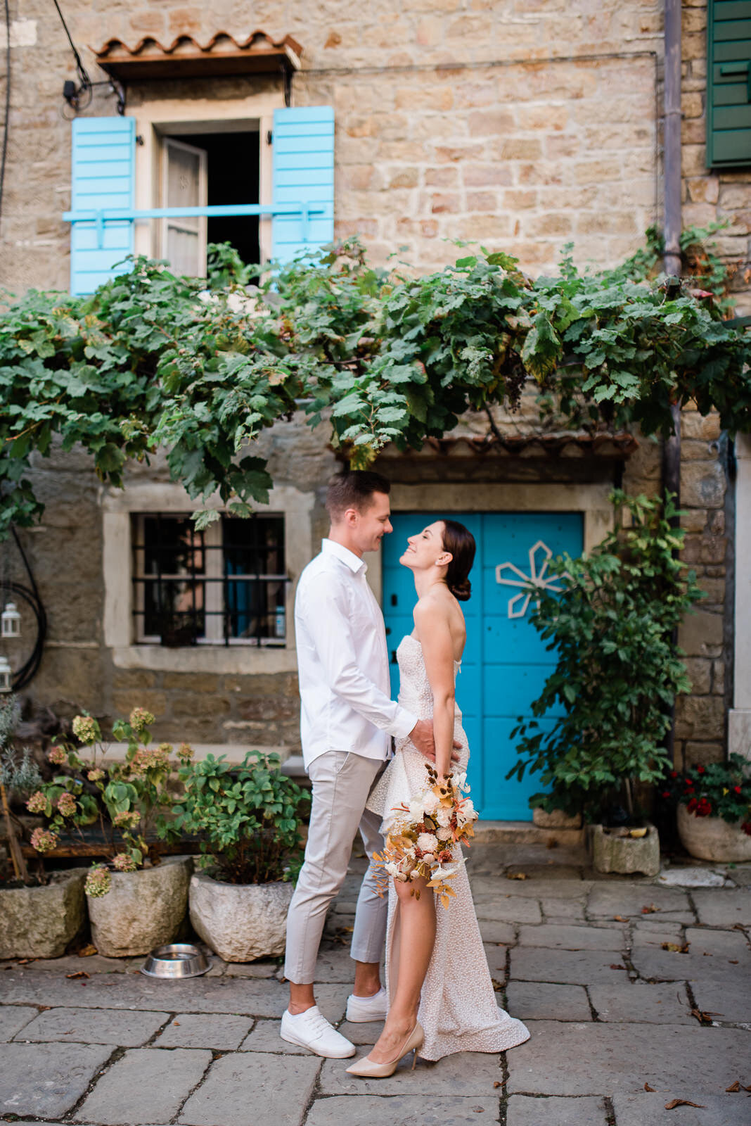 wedding couple holding bouquet standing in front of rustic house with vines and turquoise door and shutters