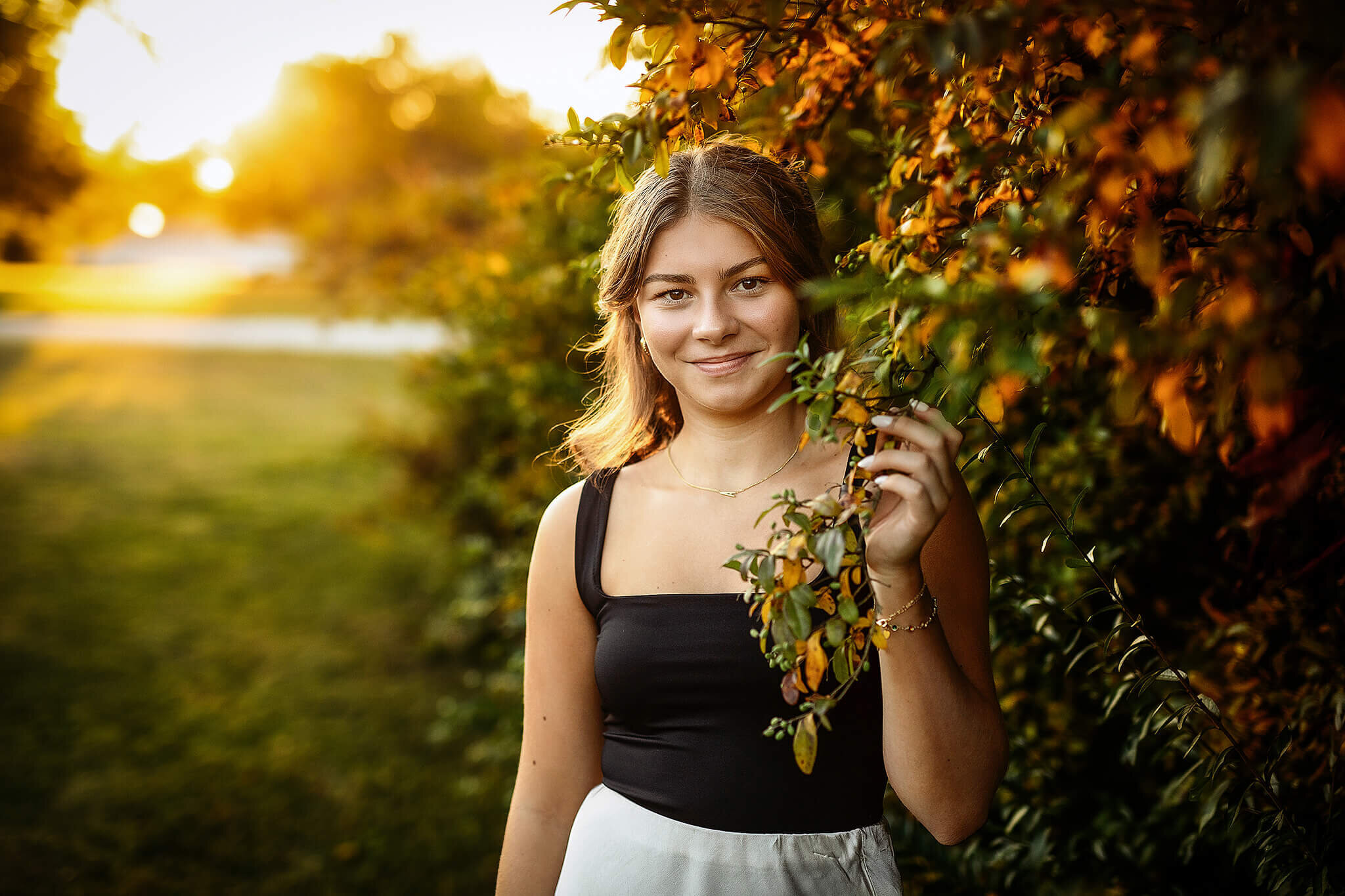 High school senior girl in pretty light standing next to a pretty colored bush