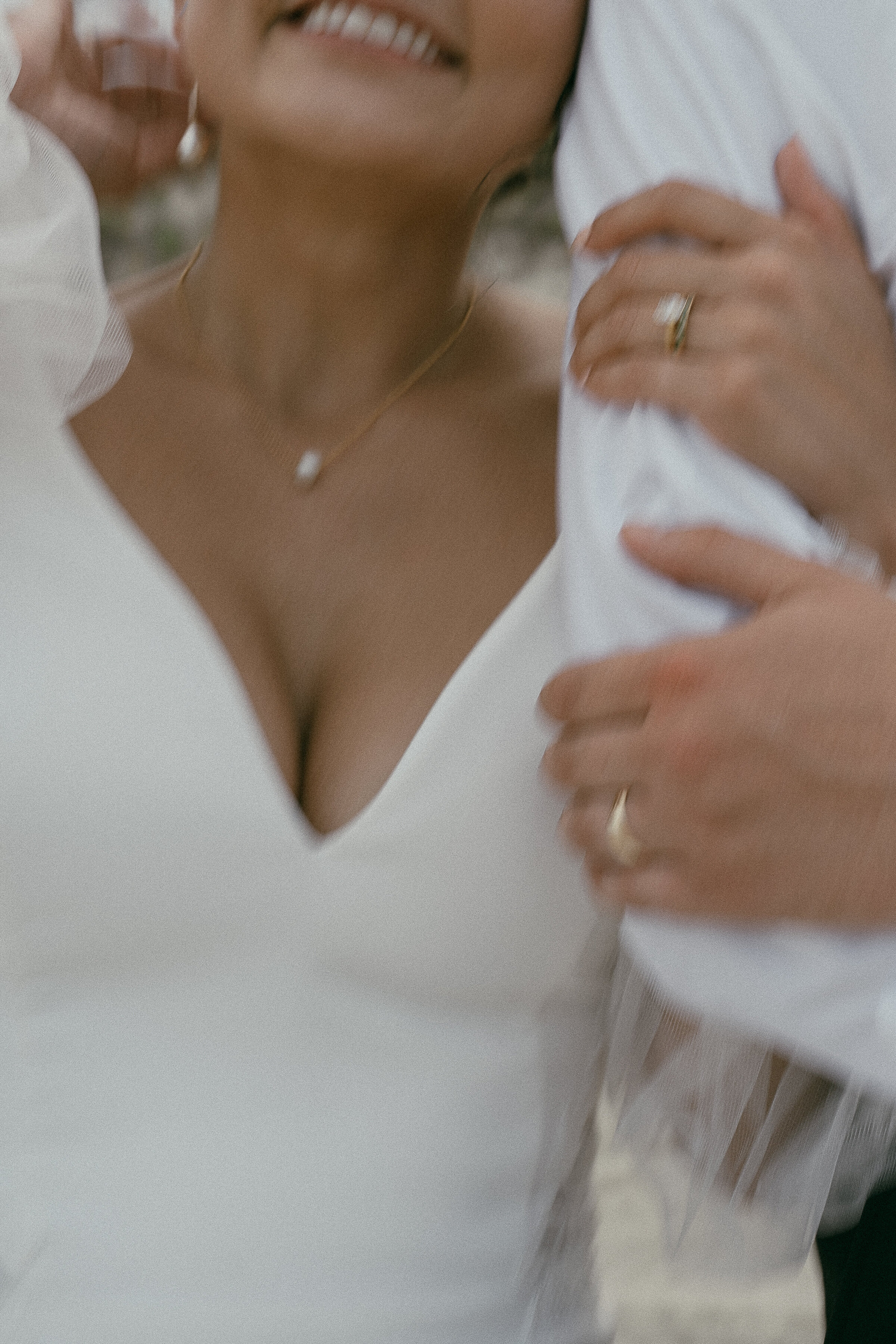 Blurred close-up of a bride smiling with the groom's hands around her.