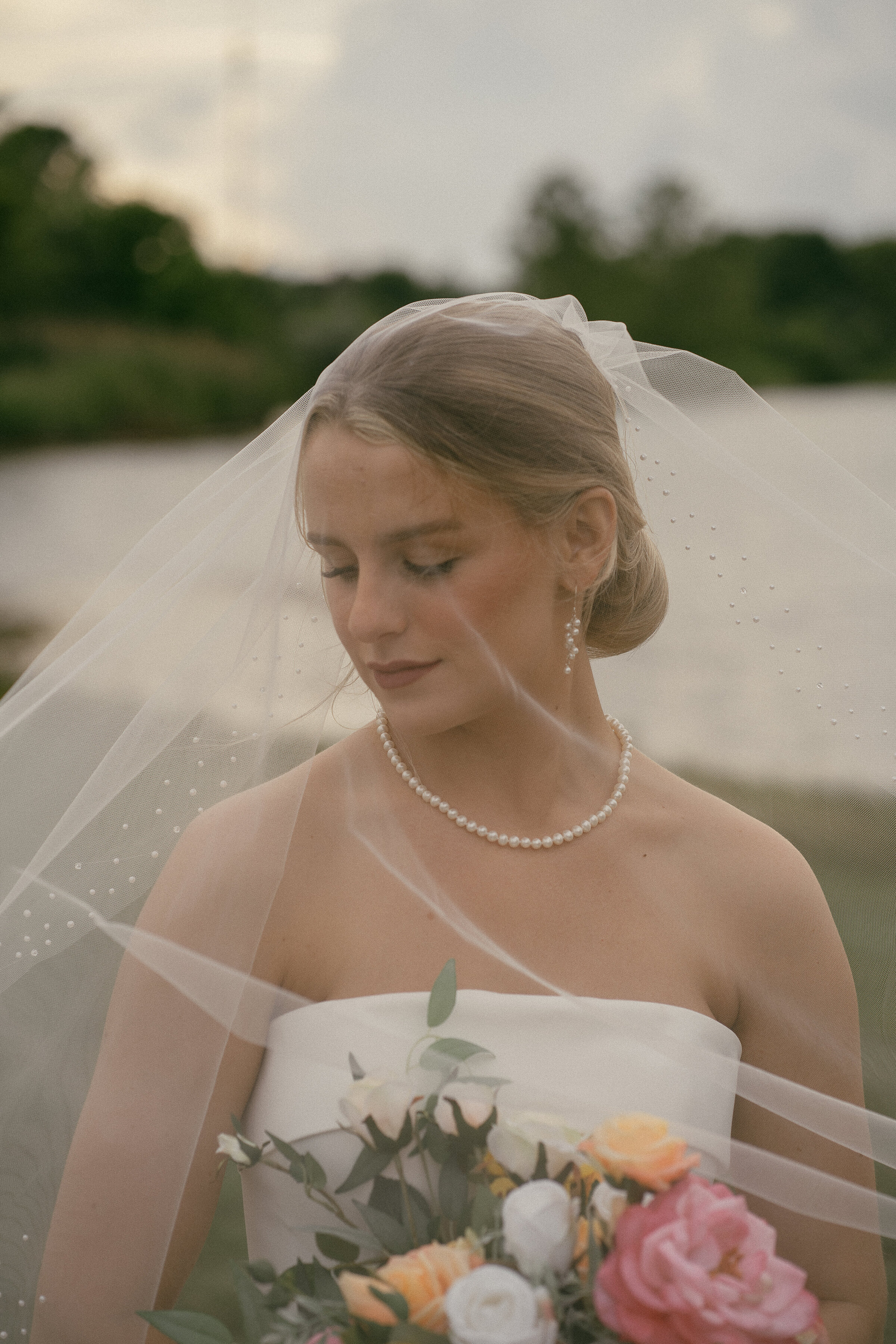Bride in a veil holding a bouquet, looking down thoughtfully.