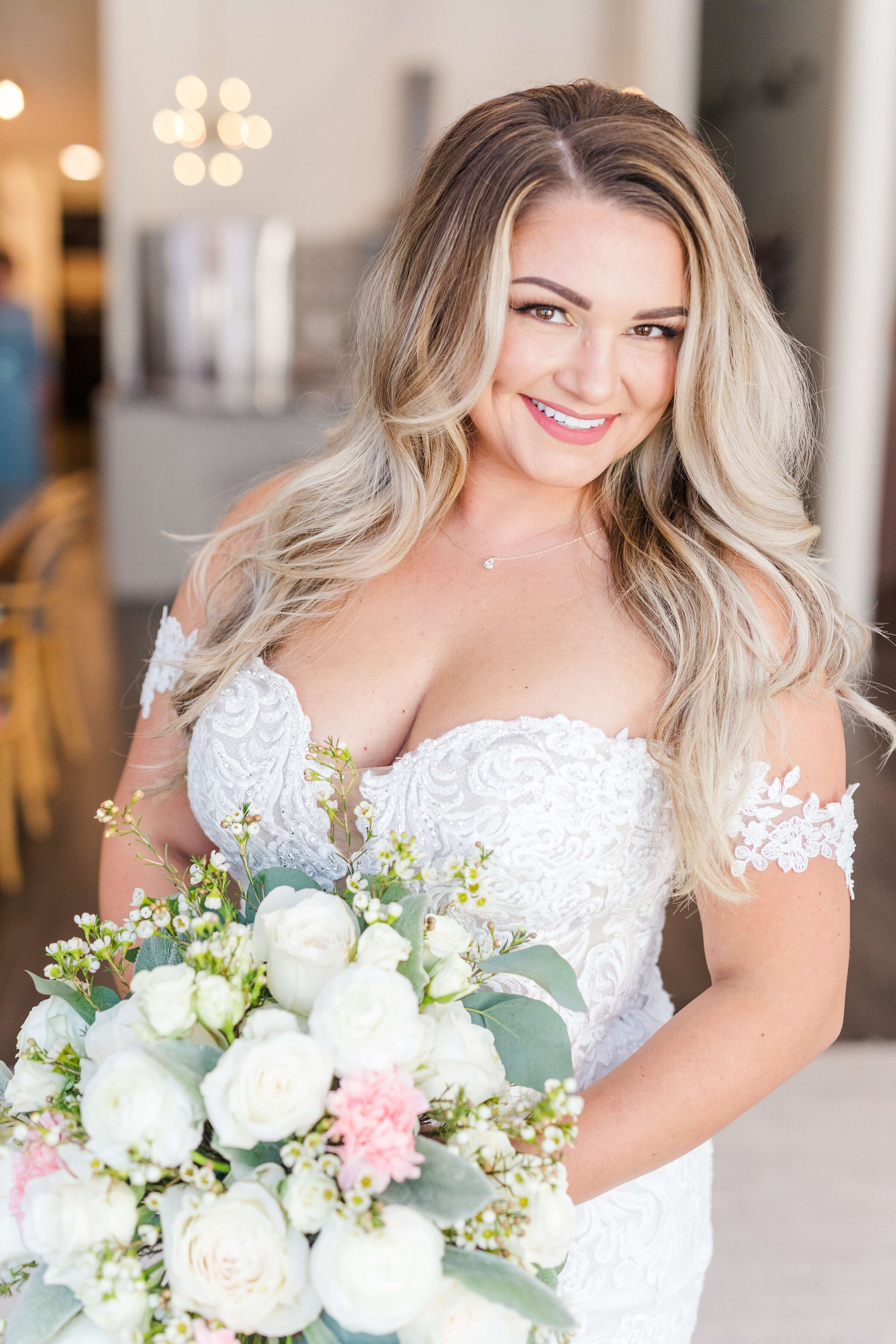 A bride holds her pink and white bouquet as she smiles at the camera.