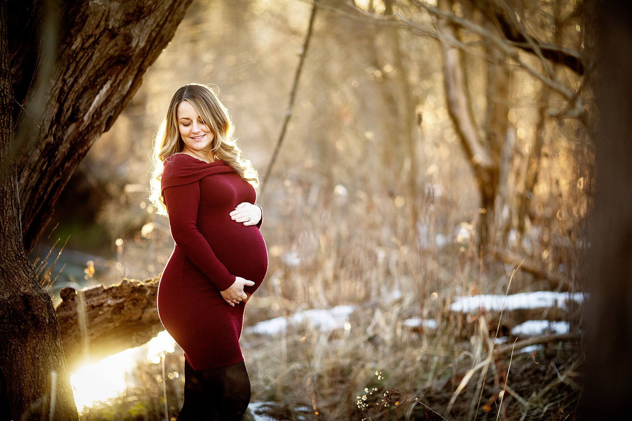 Pregnant women who is wearing a red dress standing in woods during the winter