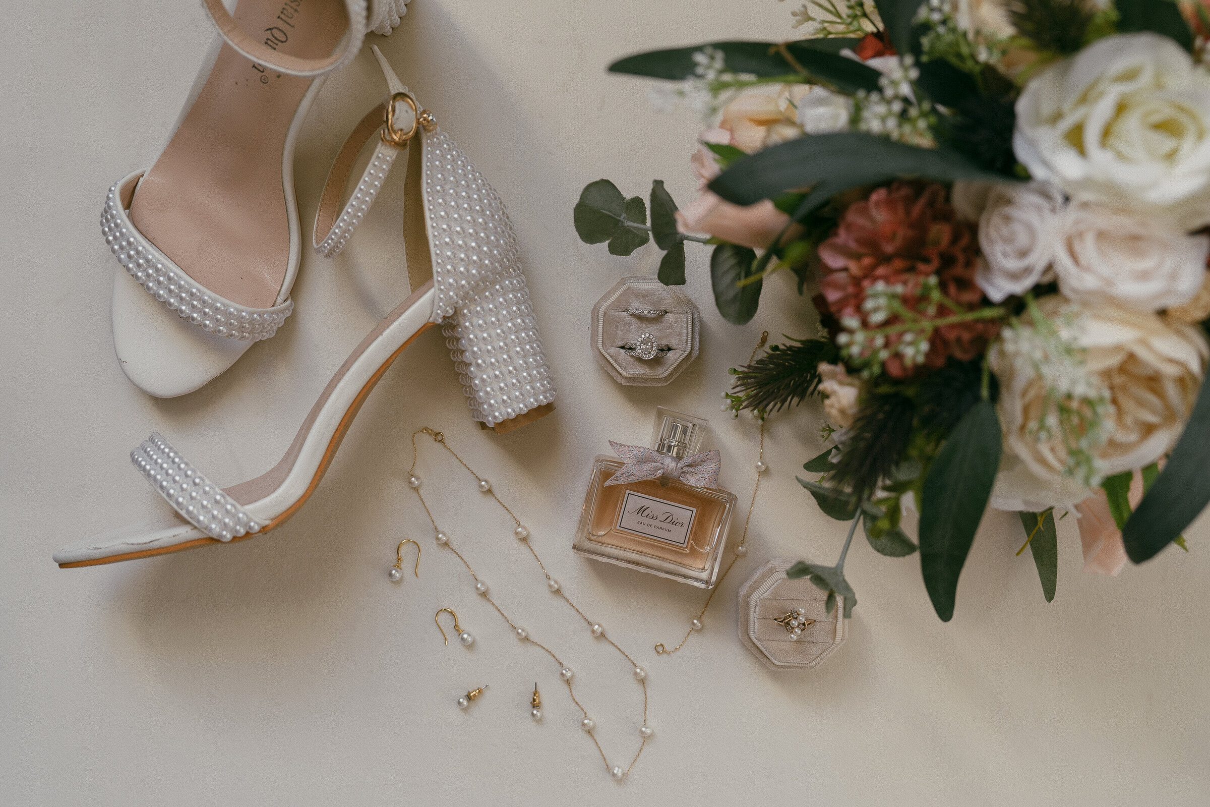 Close-up of bridal shoes and wedding ring among floral decorations.