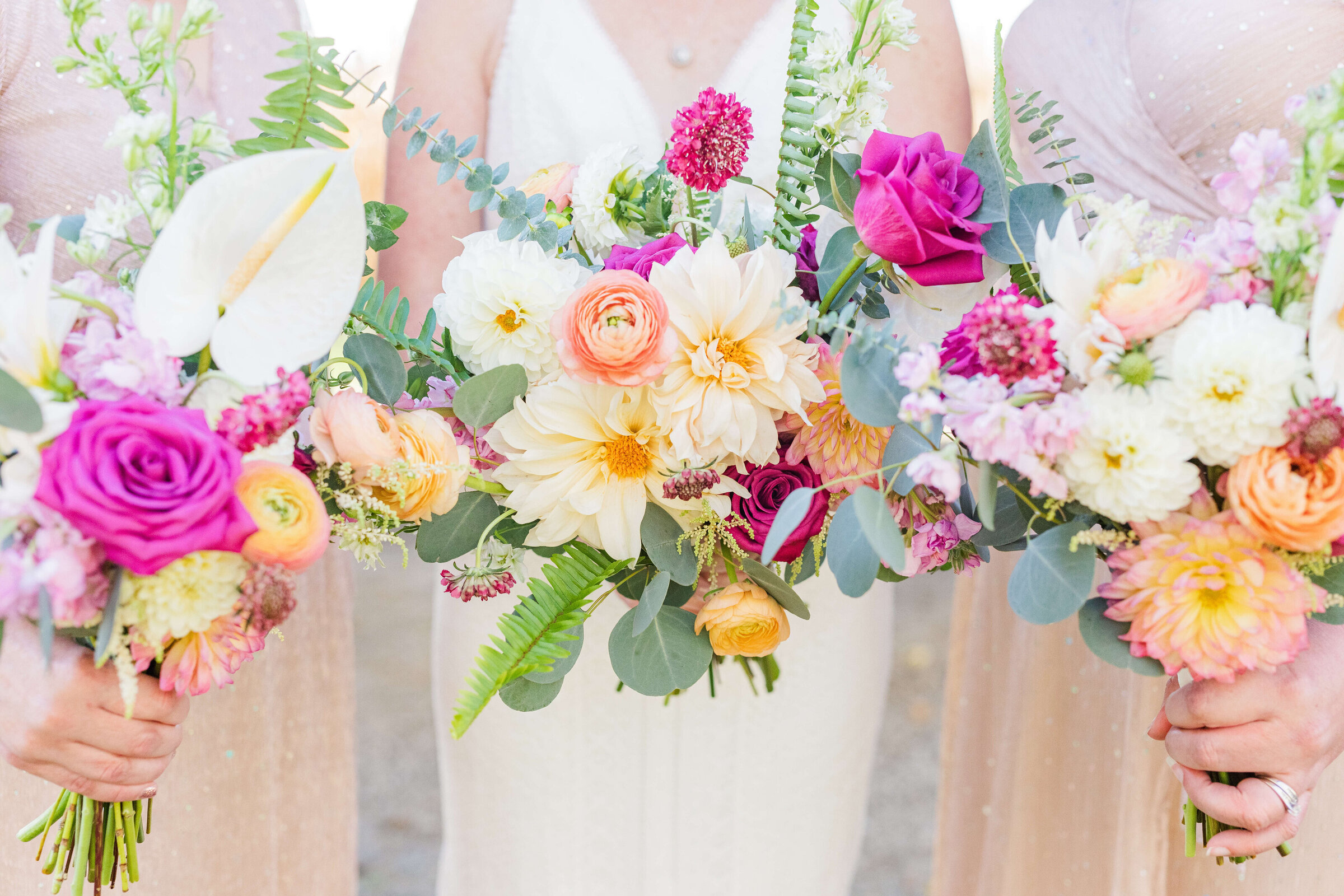 An up close photo of bridesmaids wearing pink holding their bouquets that have white, orange, and pink flowers