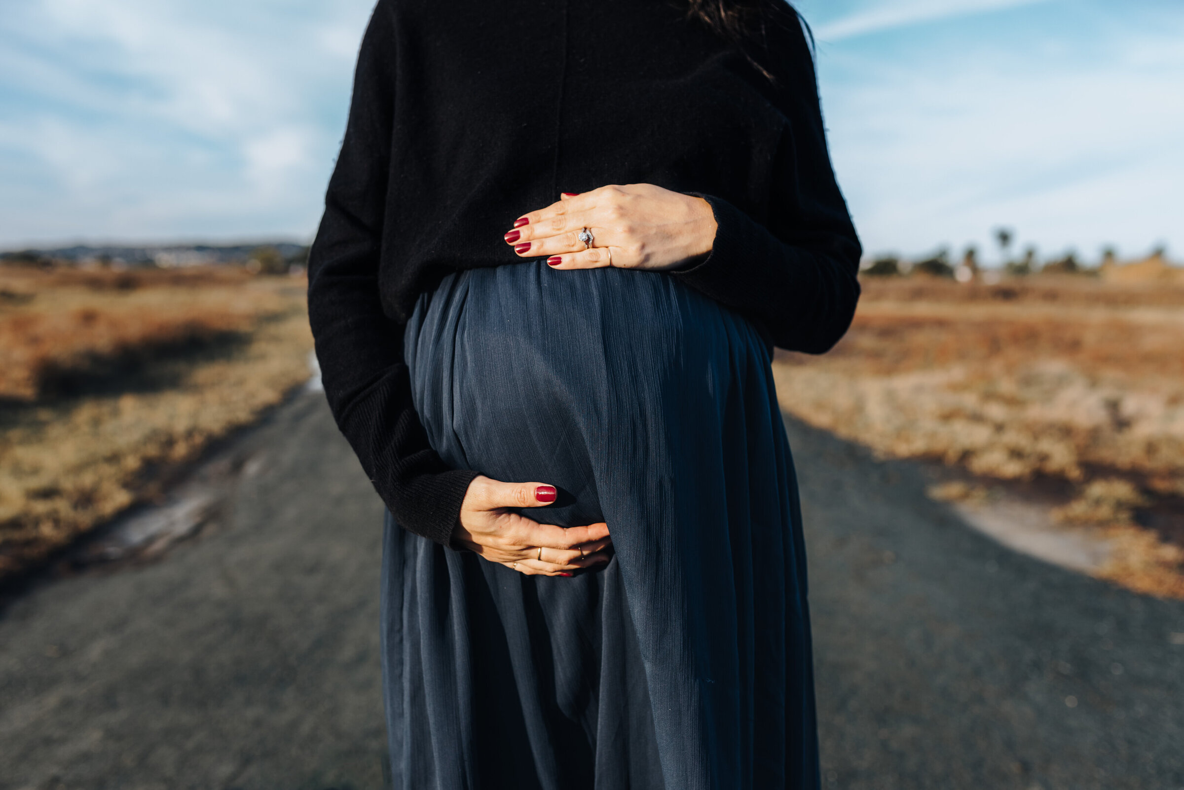 Woman holds her pregnant belly standing in the middle of the road