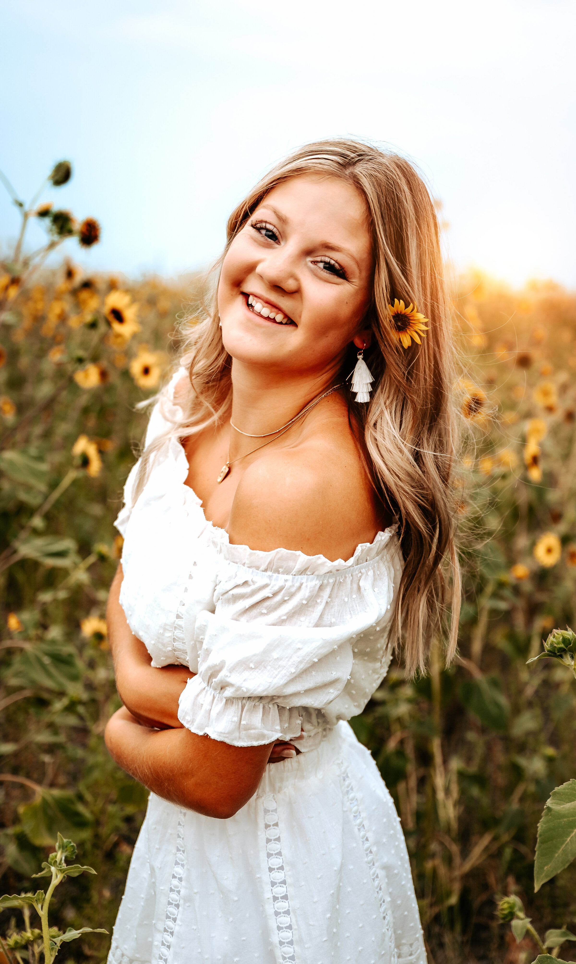 Senior girl wearing white dress has sunflower behind her ear