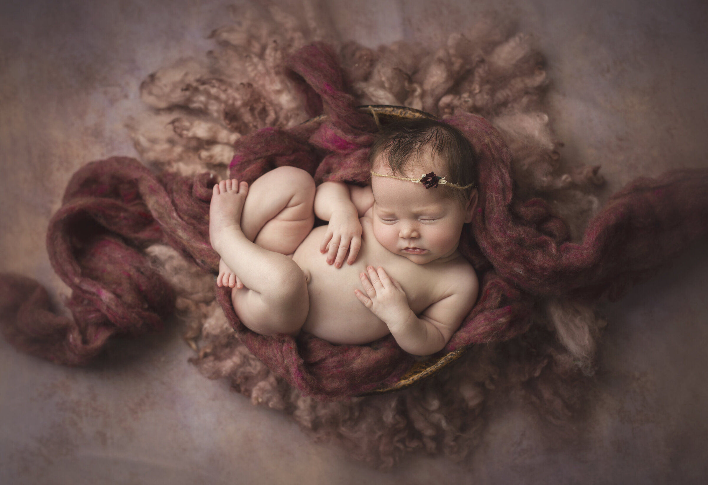 newborn baby girl laying in bowl with pretty mauve fabric and backdrop