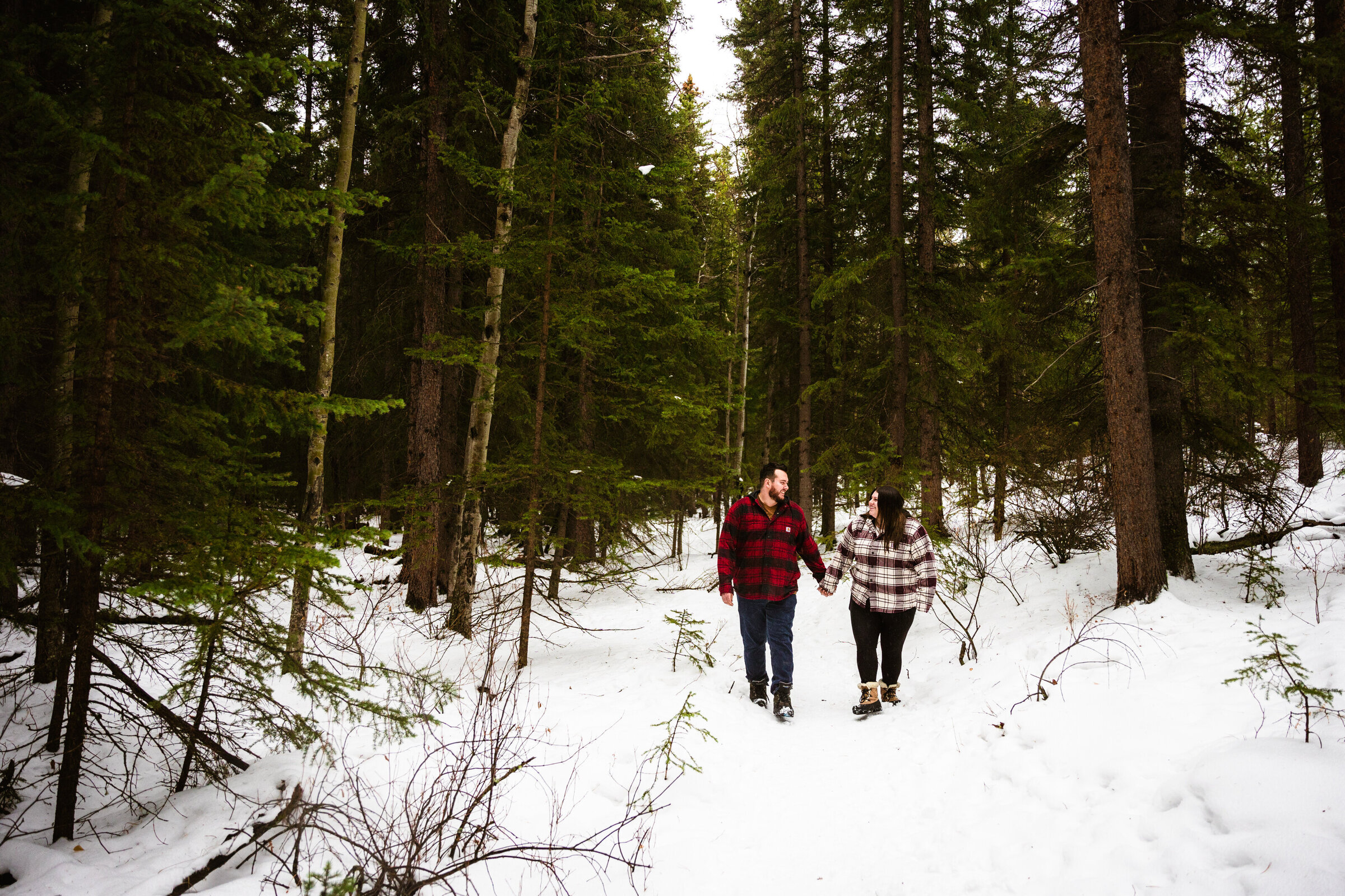 couple walk through the snowy woods for Canada engagement session