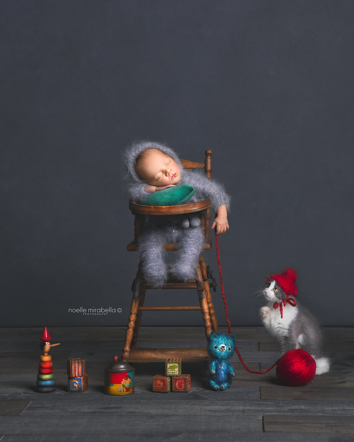 Little newborn sleeping in high chair with baby kitten playing with yarn at his feet.