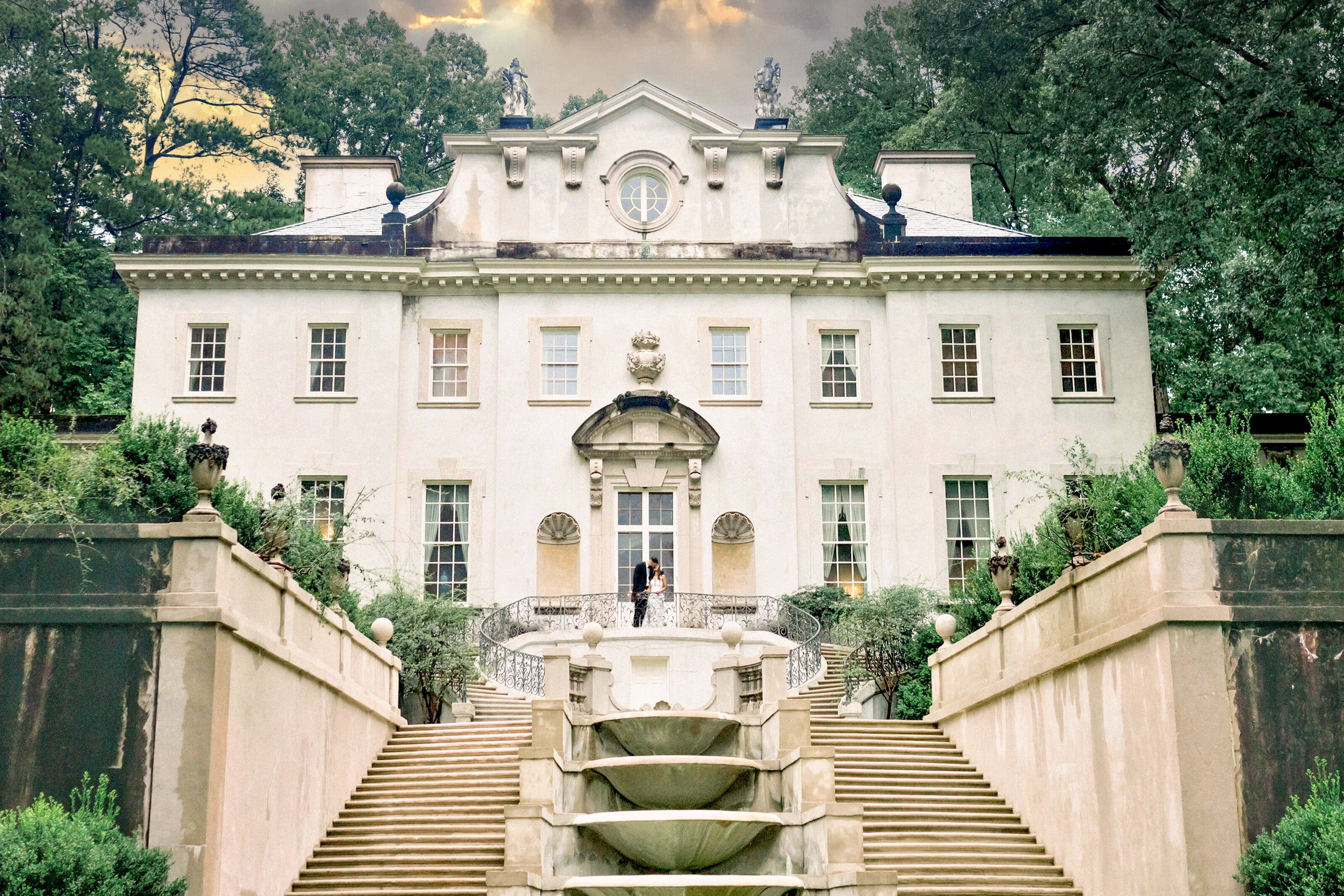 Editorial Swan House Portrait with Dramatic Clouds Editorial wide shot of bride and groom kissing in front of Swan House with dramatic cloudy sky in Atlanta