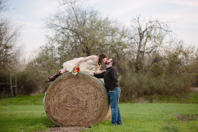 groom kissing his bride while she is on a hay bale at Hoffman Ranch wedding venue by Expose The Heart Photography