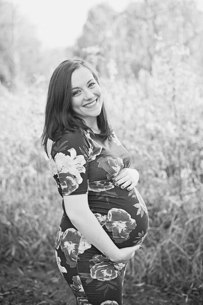 Pregnant lady smiling into camera wearing flower dress during photoshoot