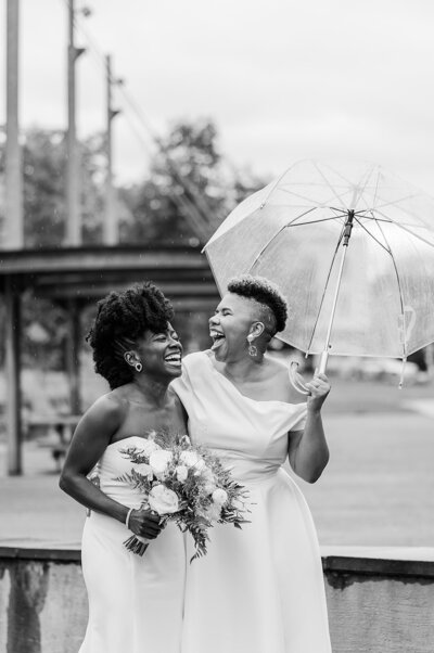 two black brides laughing in the rain in their wedding dresses