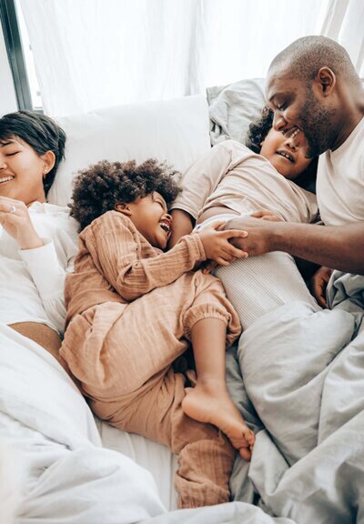 A family cozily nestled together in bed, embodying the warmth and closeness achieved through the loving principles of peaceful parenting.