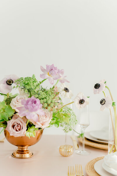 a purple and green floral centerpieces in a gold vase on a table with plates