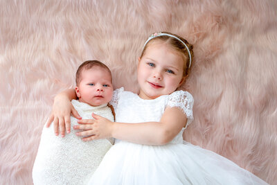 Newborn baby and big sister smiling for a sibling photo during newborn photography session by Lauren Vanier Photography