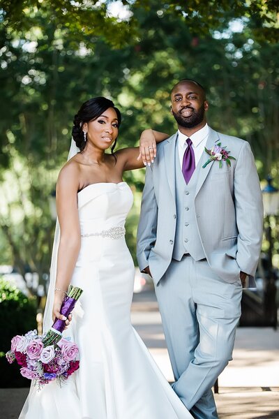 Bride and groom pose for portrait on their wedding day holding purple floral bouquet