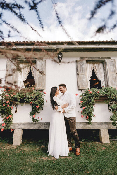bridal portrait of groom and bride hugging in front of a building with flowers in the window sill
