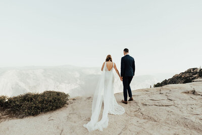 Bride and groom holding hands while standing near a cliff off the mountains