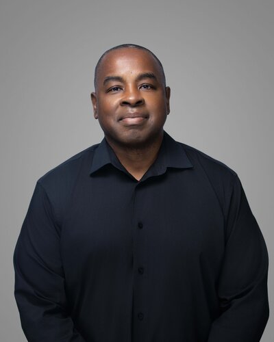 A person stands on stone steps in front of a large stone building, holding a bright red coat. They are wearing a white dress and red shoes. Trees are visible in the background.